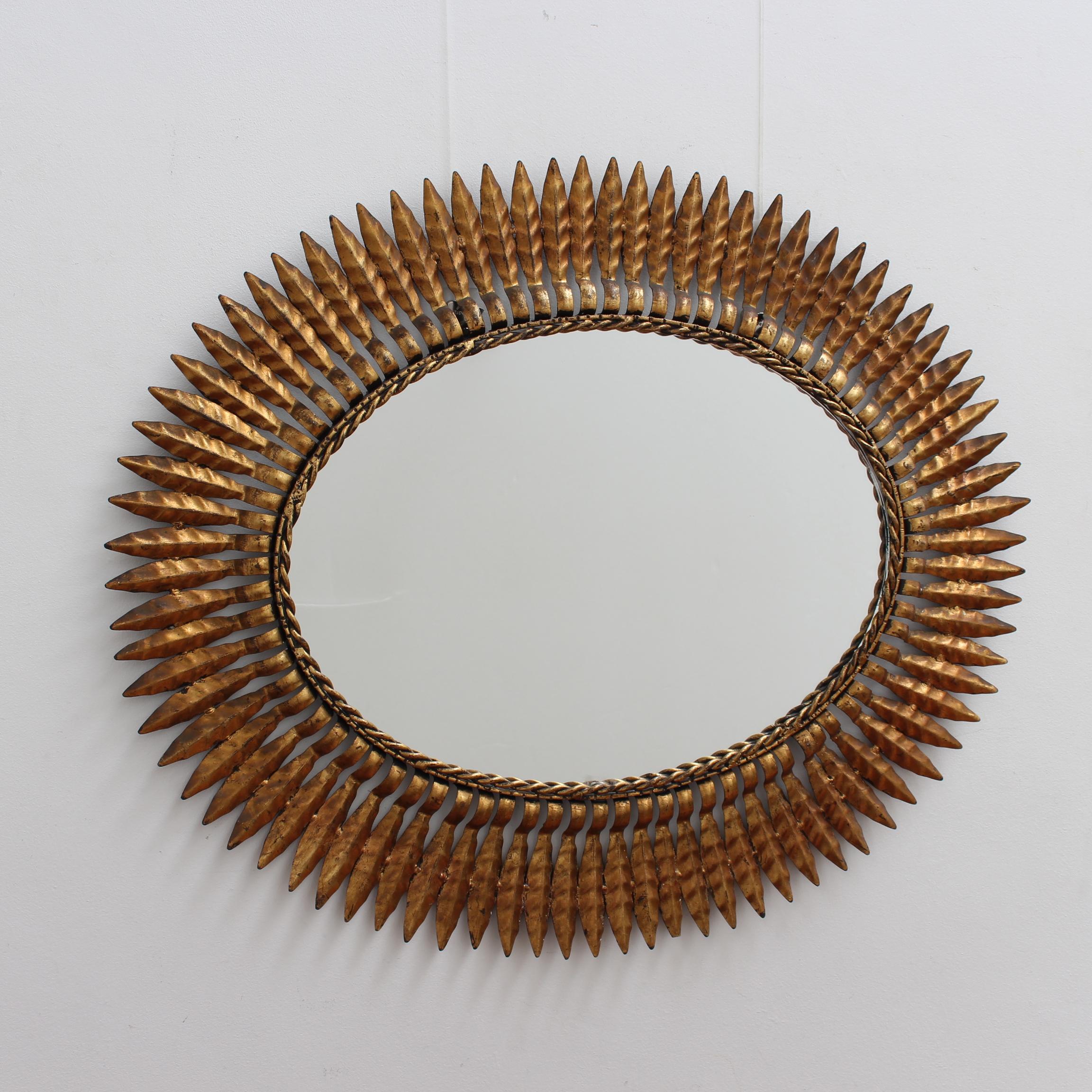 Spanish vintage gilt metal sunburst mirror (circa 1960s) with leaf motif rays and rope-pattern mirror border. Some authentic age spots and characterful markings appear on gilt surface adding to its presence while reflecting its true age and history.