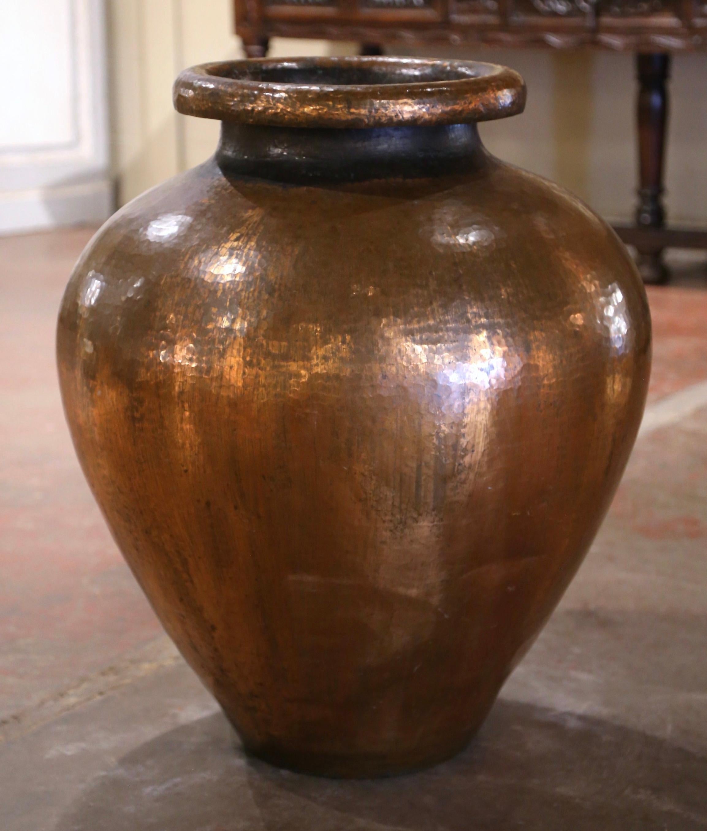 Decorate a room with vintage copper urn-shape planter. Crafted in Spain circa 1950 and built of hammered copper, the planter features a wide, slightly flared rim and a narrow neck, which smoothly transitions into the larger, bulbous body. Its