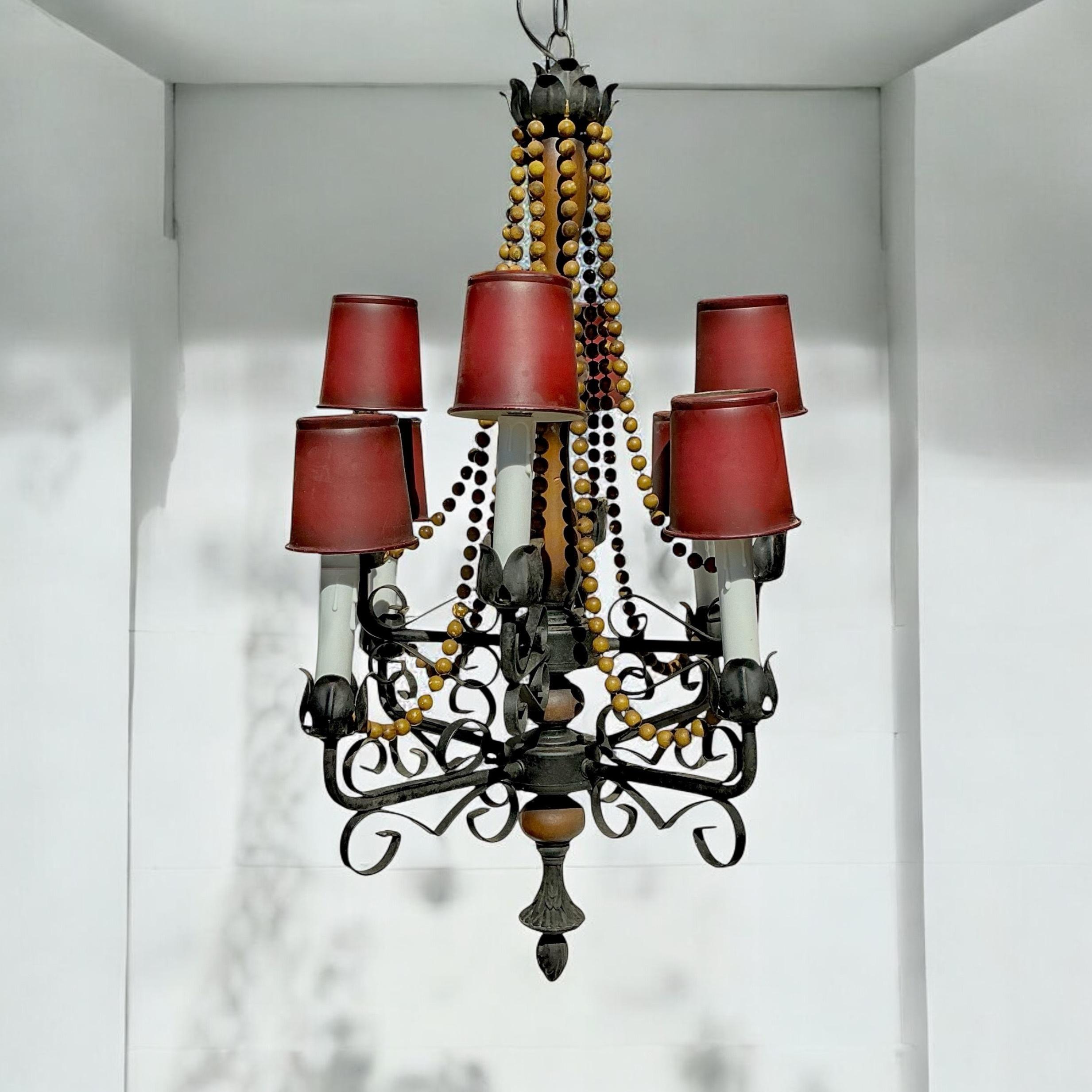 This is a mid-century Spanish iron chandelier with a carved fruitwood core and cascading beads. The tole shades are original, and the fixture would look nice without the shades too. There is about 8 feet of chain. All fixtures are checked by a