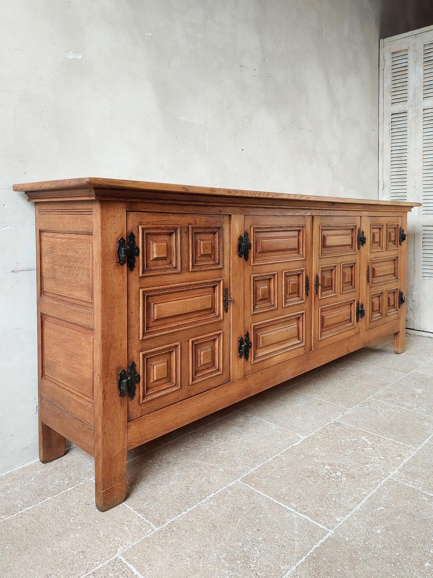 Midcentury Spanish oak sideboard, 1950s. Beautiful solid oak sideboard in Spanish rustic modernist style. With four doors decorated with geometric panels and wrought iron hardware. A spacious interior with shelves across the width and two drawers.