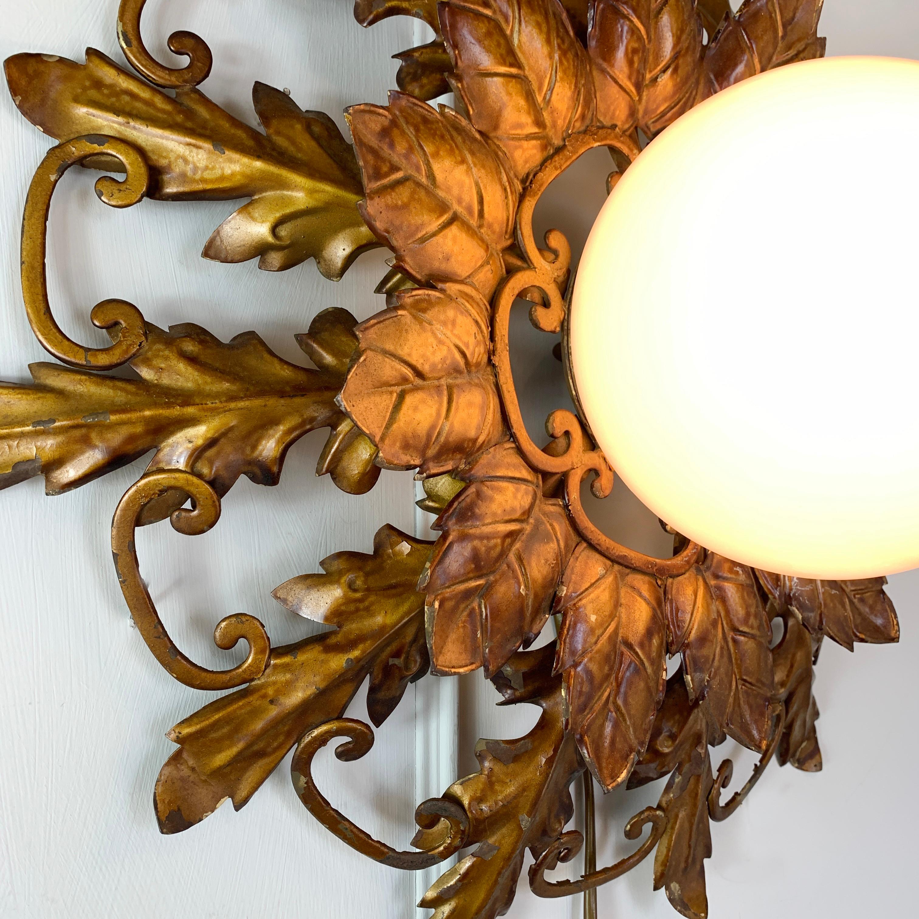 A beautiful and ornate Spanish iron work sunburst light that could be used either on a ceiling or wall, hand finished in antique gold, with a single central lamp holder that sits behind the glass globe lamp cover. Very well proportioned and in
