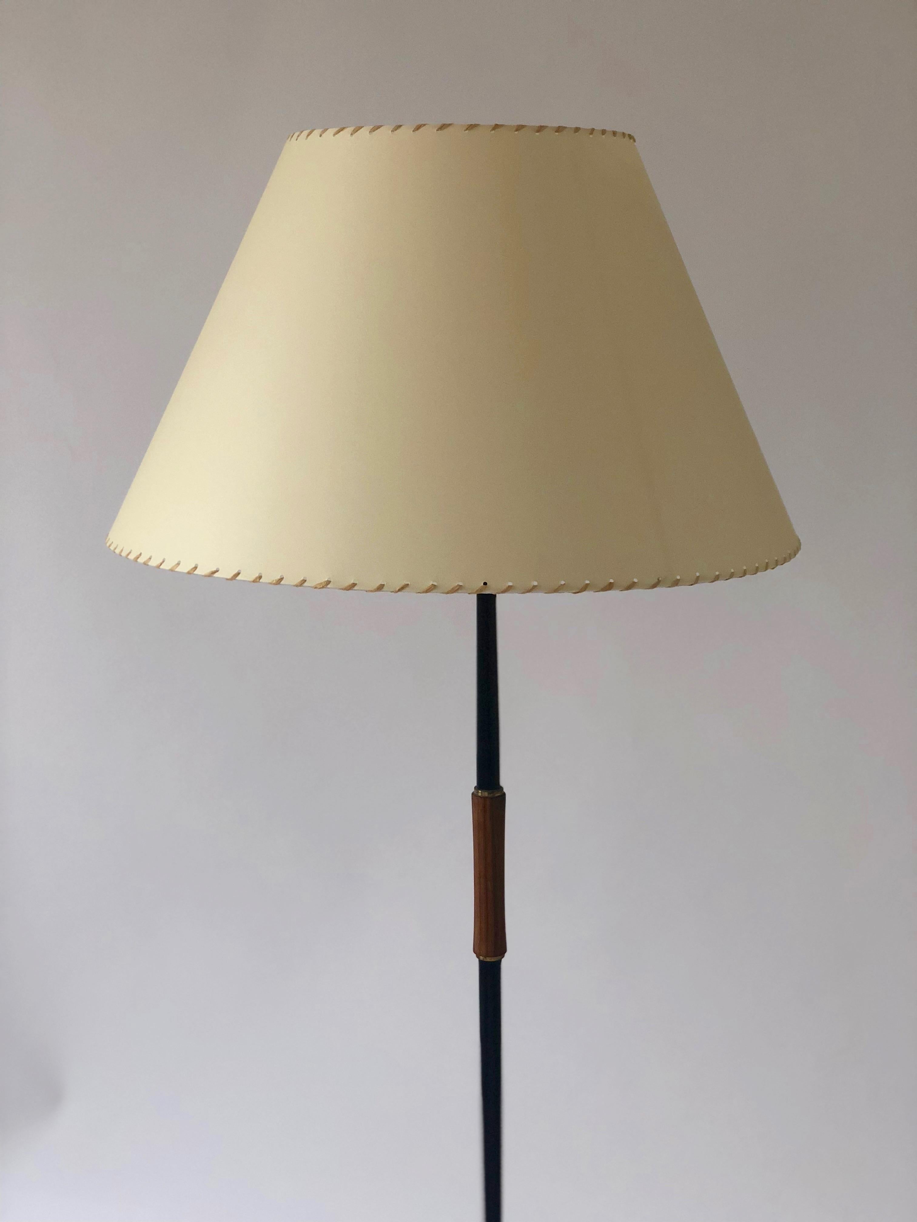 Elegant lampadaire en métal patiné noir, avec poignée en bois de teck et détails en laiton.
L'abat-jour est fabriqué d'après l'original en papier et en sisal.
La lampe est recâblée.