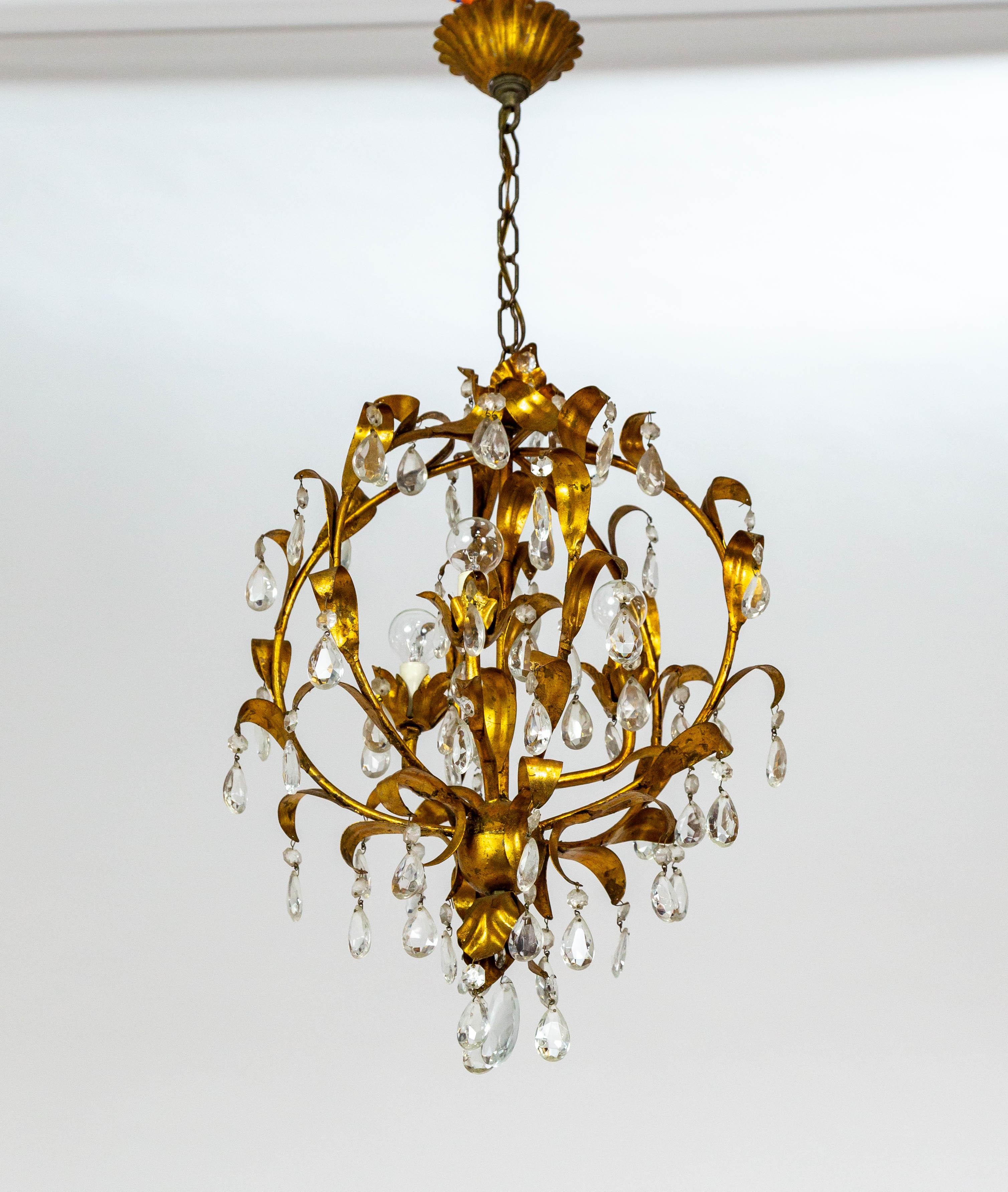 An Italian, gilt metal chandelier in a spherical cage shape. The curling leaves lining the structure dangle octagonal and pendalogue crystals. It has three interior lights (candelabra sockets). A beautiful design. Newly rewired with matching chain