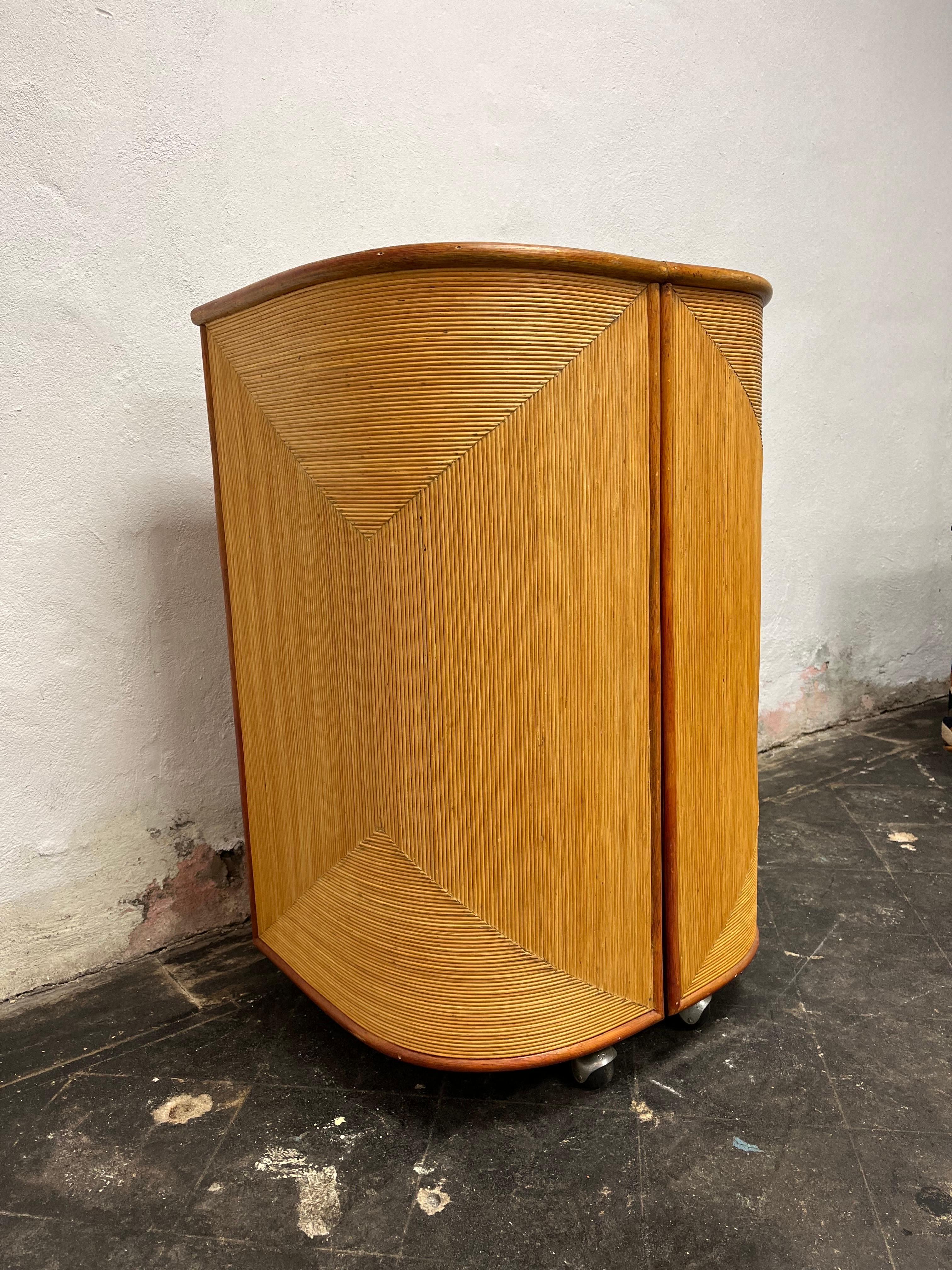 Unbelievably stylish mid century dry bar. Split reed and bamboo. Compact bar cabinet,  in the style of Paul Frankl, swings wide to expose ample storage for you barware. Split reeded designed exteriro with thick bamboo or rattan trim. Sits on brass