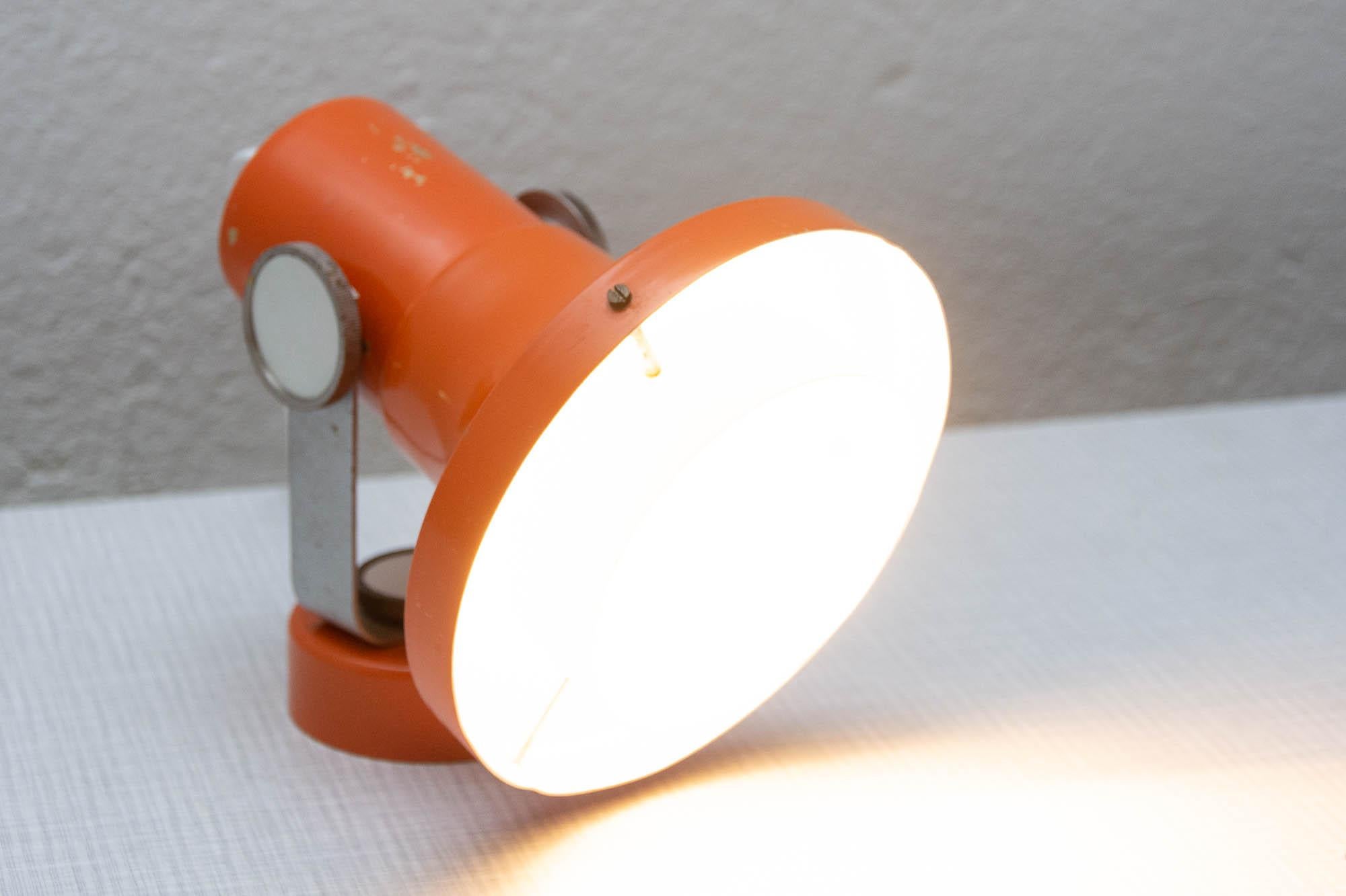 This table lamp or spot light was designed by the Czech architect Pavel Grus for Kamenicky Senov company in the 1960s. The inclination of the head are adjustable. This metal lamp is painted in orange is in good vintage condition with slight marks of