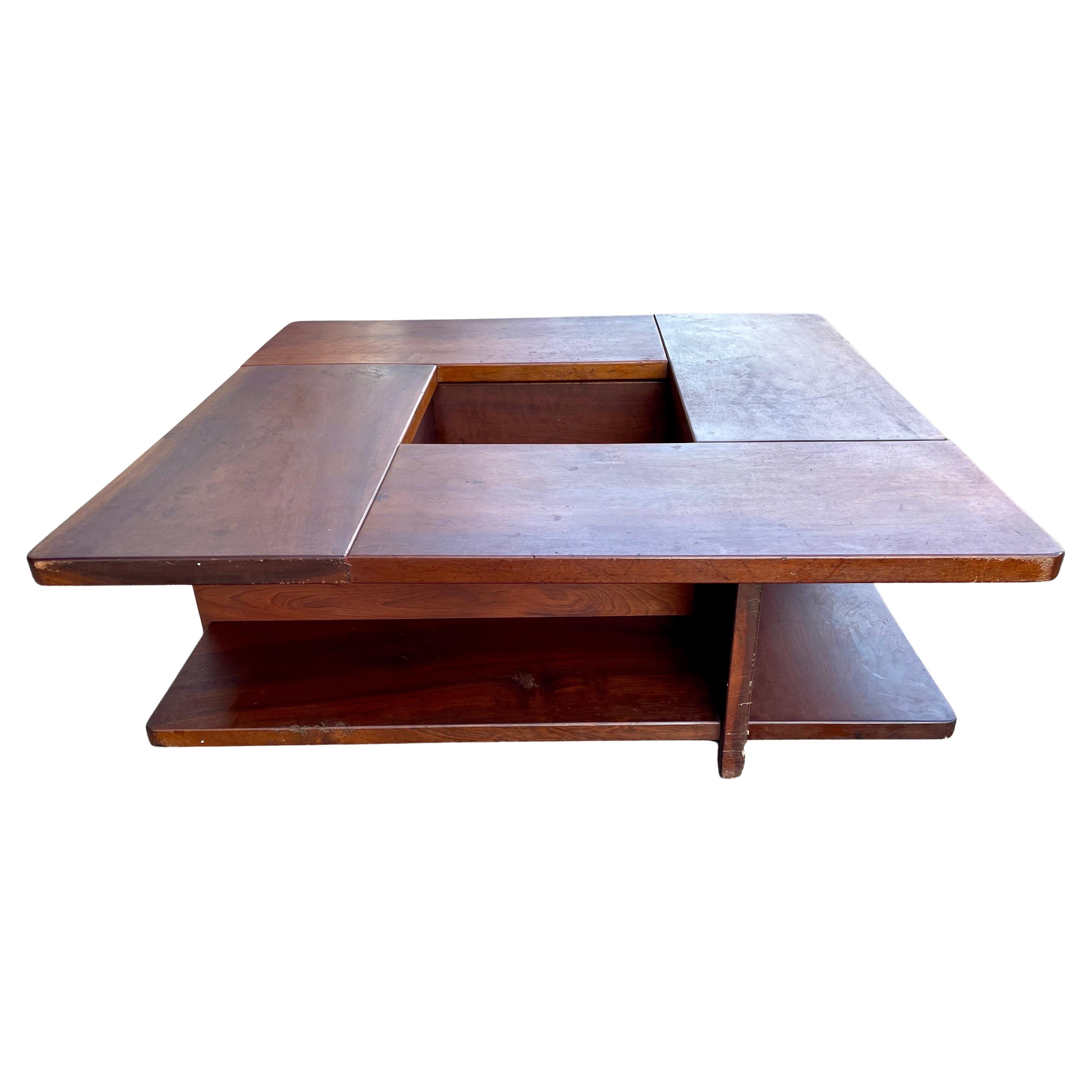 This is a fantastic solid wood, heavy (Walnut maybe?) square coffee table with an interesting center cut-out. The cut-out has supports at the bottom that may be original or added and may have supported a lining or a shelf. The top is supported on