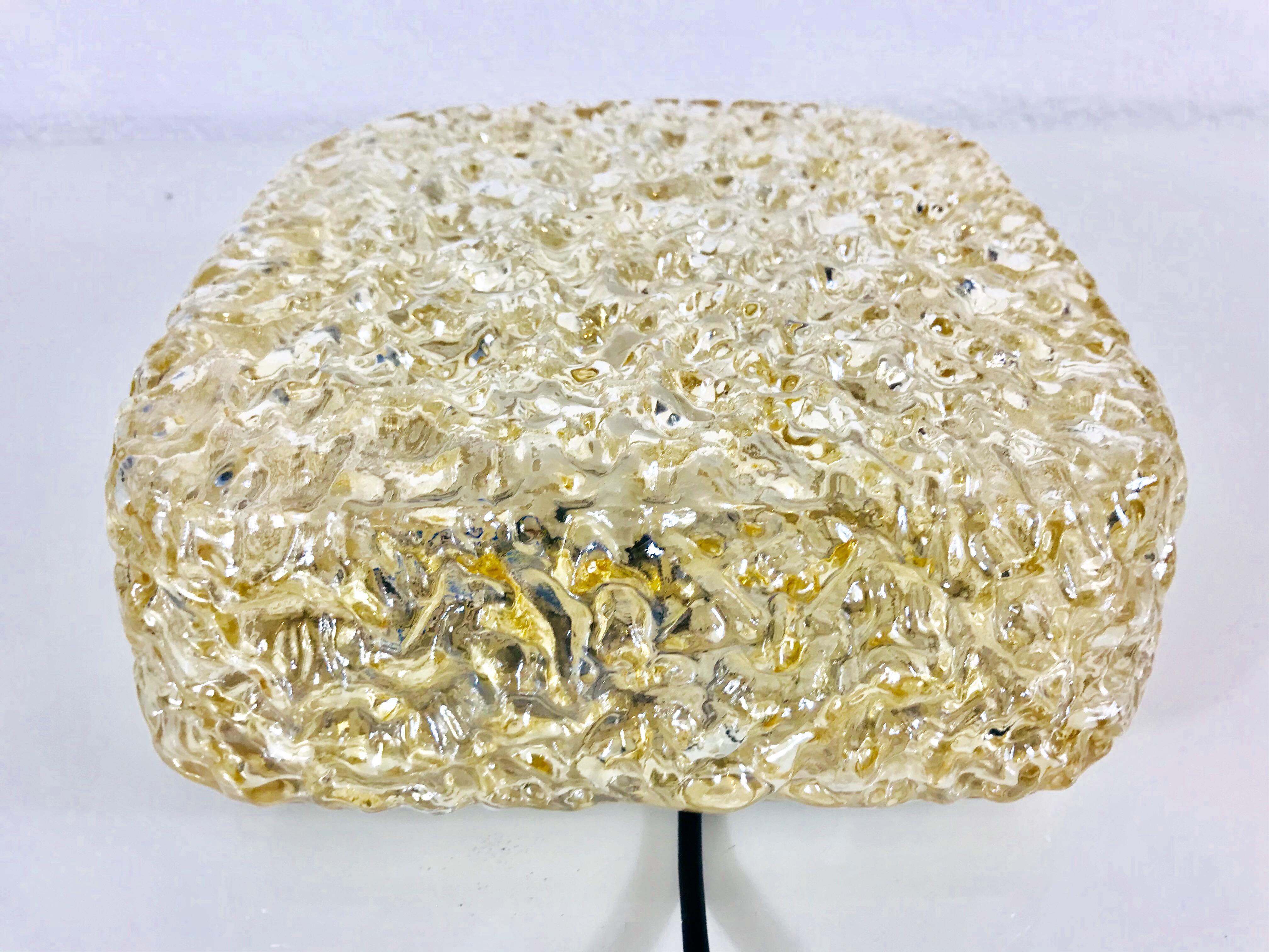 A Mid-Century Modern flush mount by the German brand Glashütte Limburg. It has a square shape and is made of crystal glass and brass. The glass shade is structured.

The light requires one E27 light bulb.