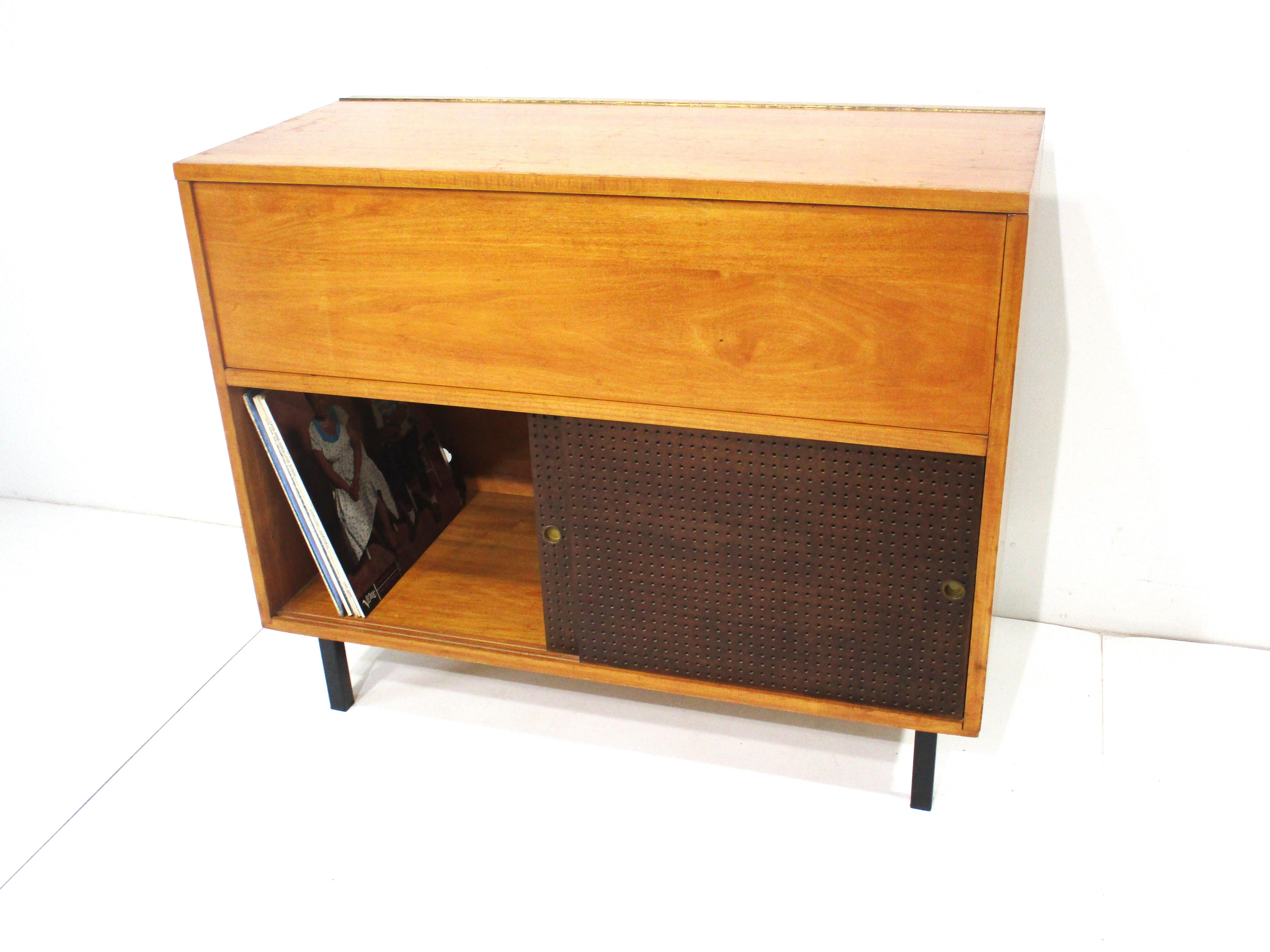 A honey toned solid maple stereo cabinet with pull up top revealing an area for your stereo and turntable having pre cut holes for wiring . The lower area has two perforated sliding doors and storage that will fit your vinyl collection . Sitting on