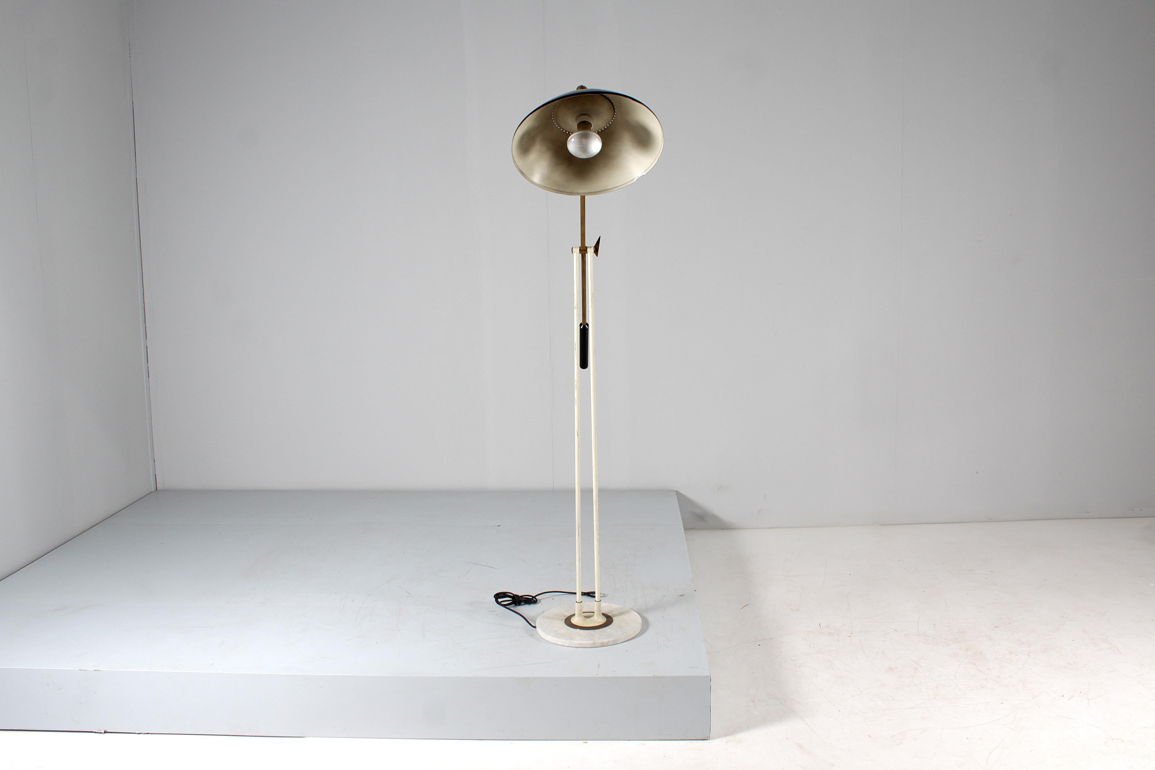 Stylish floor lamp with adjustable and directional rocker in golden brass, diffuser in black lacquered metal with perforated circumference, vertical support in white painted metal on a circular base in white marble with a banded circumference in