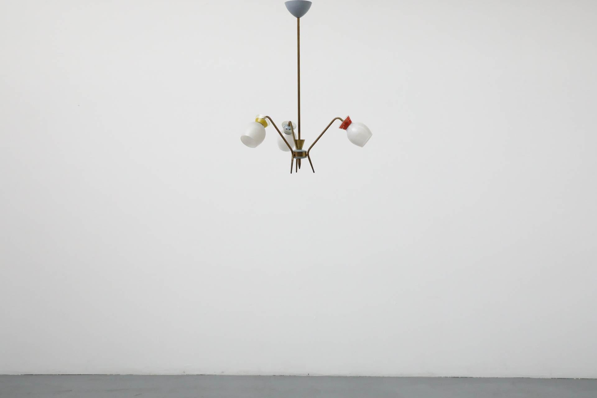 Adorable Stilnovo inspired 3 arm chandelier. This piece is loaded with character and fun details. It features a brass frame with multi-color banded glass shade details in red, yellow and grey with pale blue enameled accents and petal-like socket