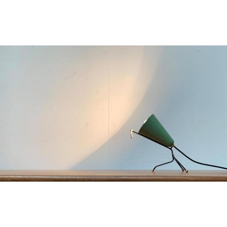 Mid Century table lamp with a characteristic umbrella and foot.

A design of French or Italian origin. An elegantly curved foot made of black -painted steel bars carries the umbrella. The ends of the frame are completed with brass detail. The