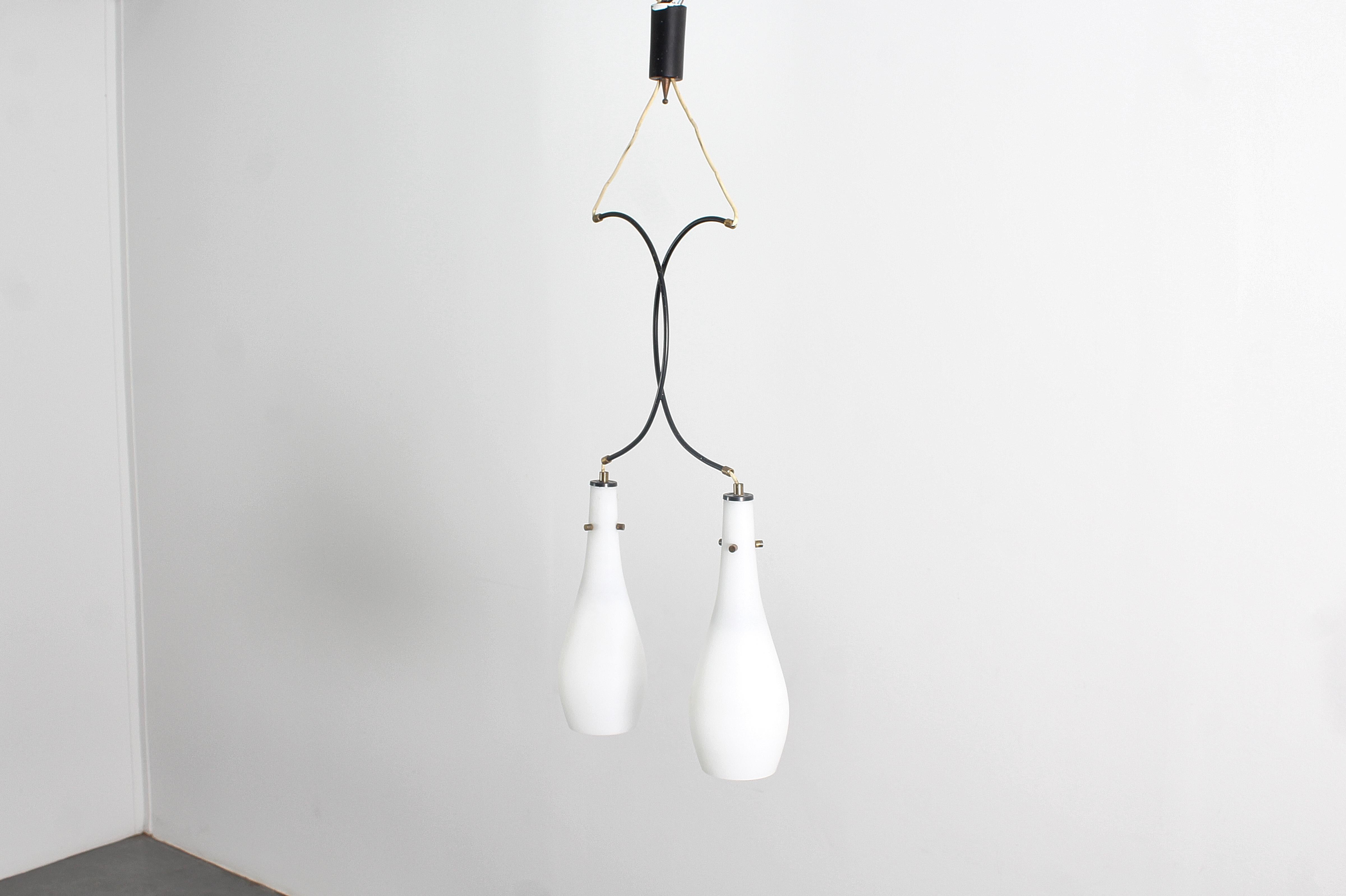 Una lampada a sospensione di grande effetto con due diffusori in vetro opalino, supporti in metallo curvato e finiture in ottone. Nello stile di Stilux Milano, prodotto in Italia negli anni Sessanta. Se coerente con l'età e l'uso.