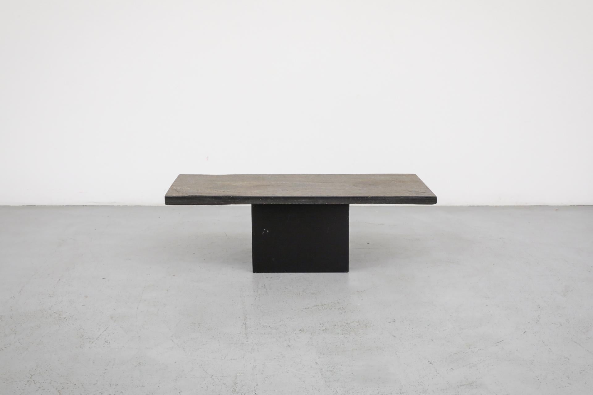 Mesa de centro o auxiliar de mediados de siglo con grueso tablero de piedra que se asienta libremente sobre una base cuadrada de acero esmaltado negro, de Metaform. En estado original con desgaste visible, incluidos arañazos en el esmalte. Desgaste