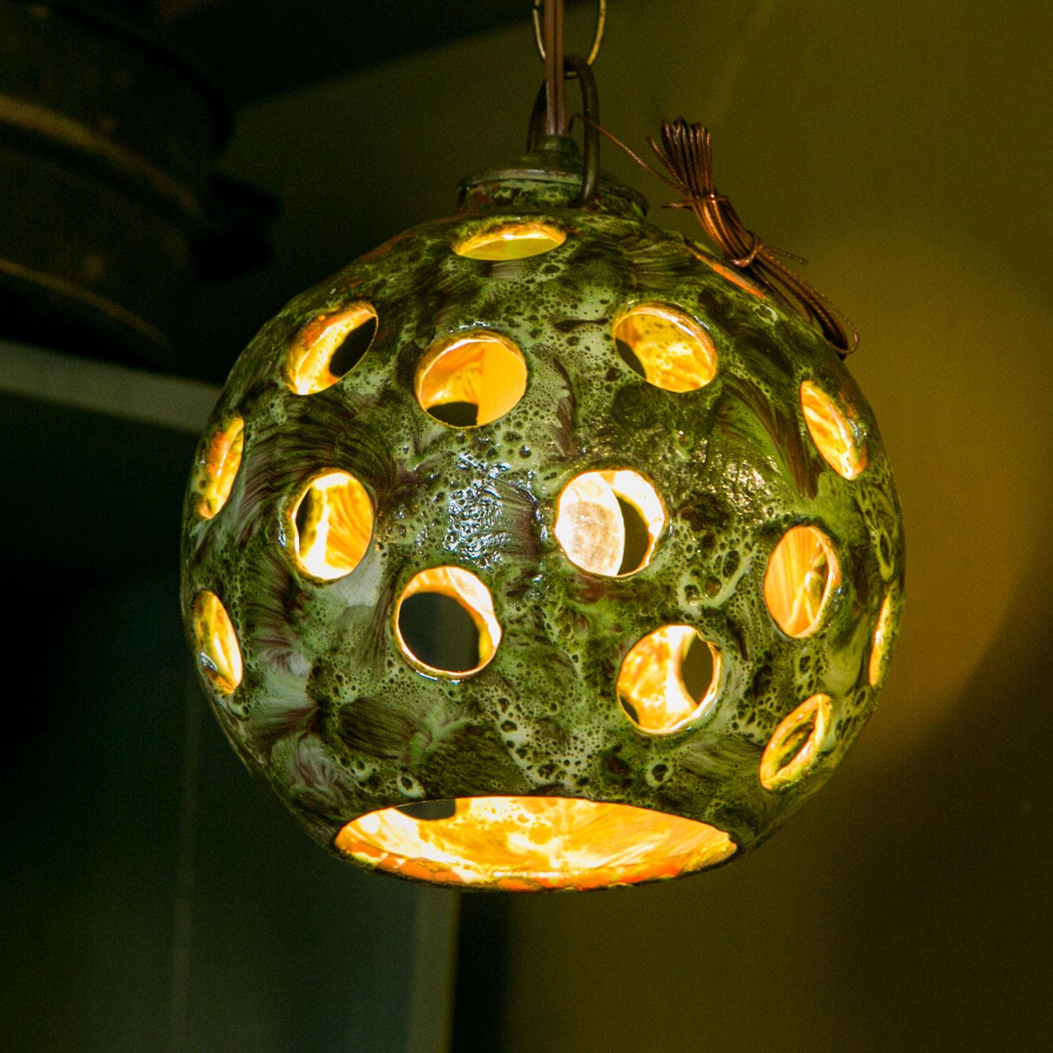 Mid-century stoneware pendant light from Germany. Ceramic surface is a nice textured multi-hue green. The pierced circles create wonderful shadows and movement upon the wall. This one-of-a-kind light evokes an Arts and Crafts or Bohemian feel. Newly