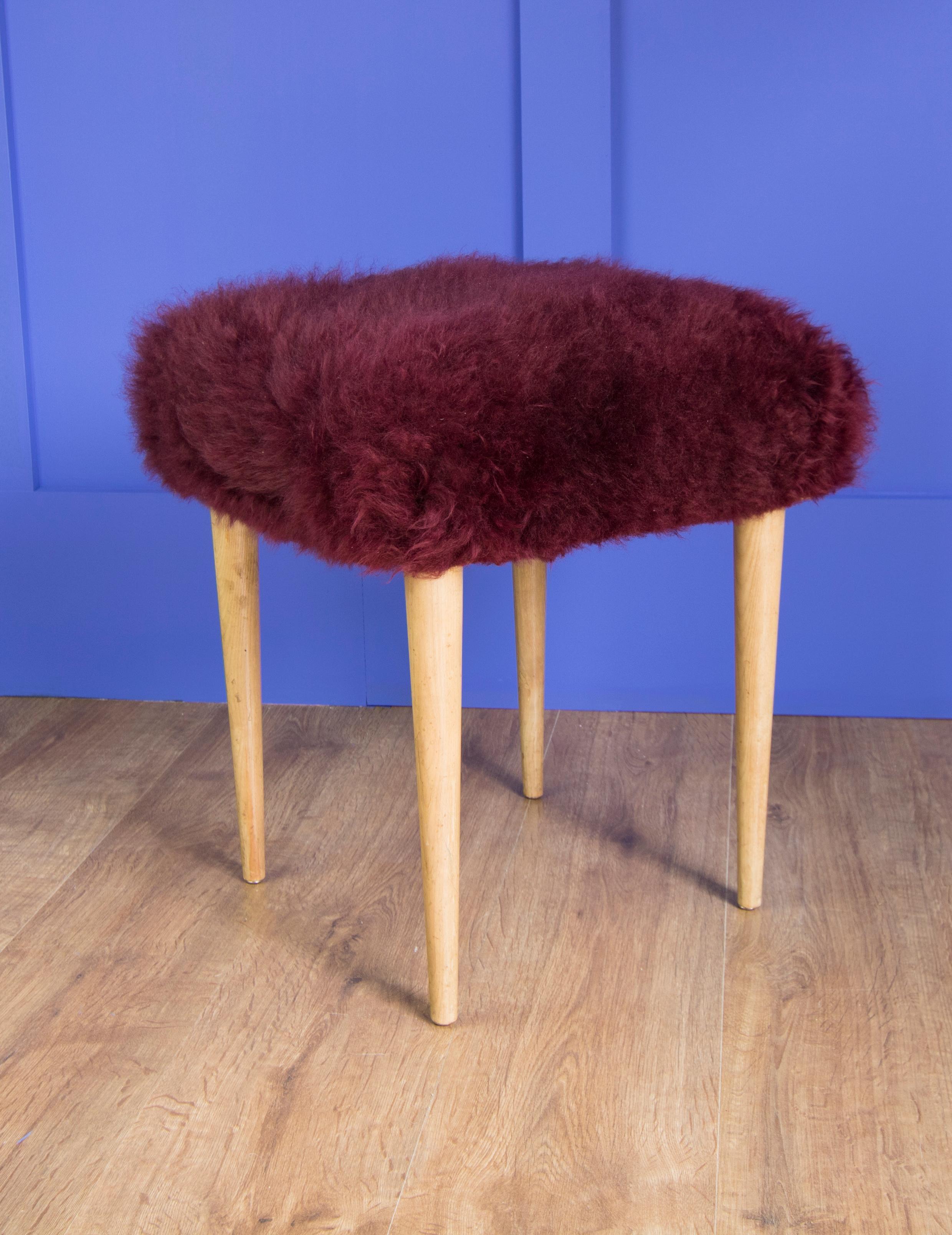 This little stool has been sympathetically restored to its former midcentury glory with vintage burgundy sheepskin. Pale wood legs. Luxuriously dense sheepkin super soft finish in this unusual color.
