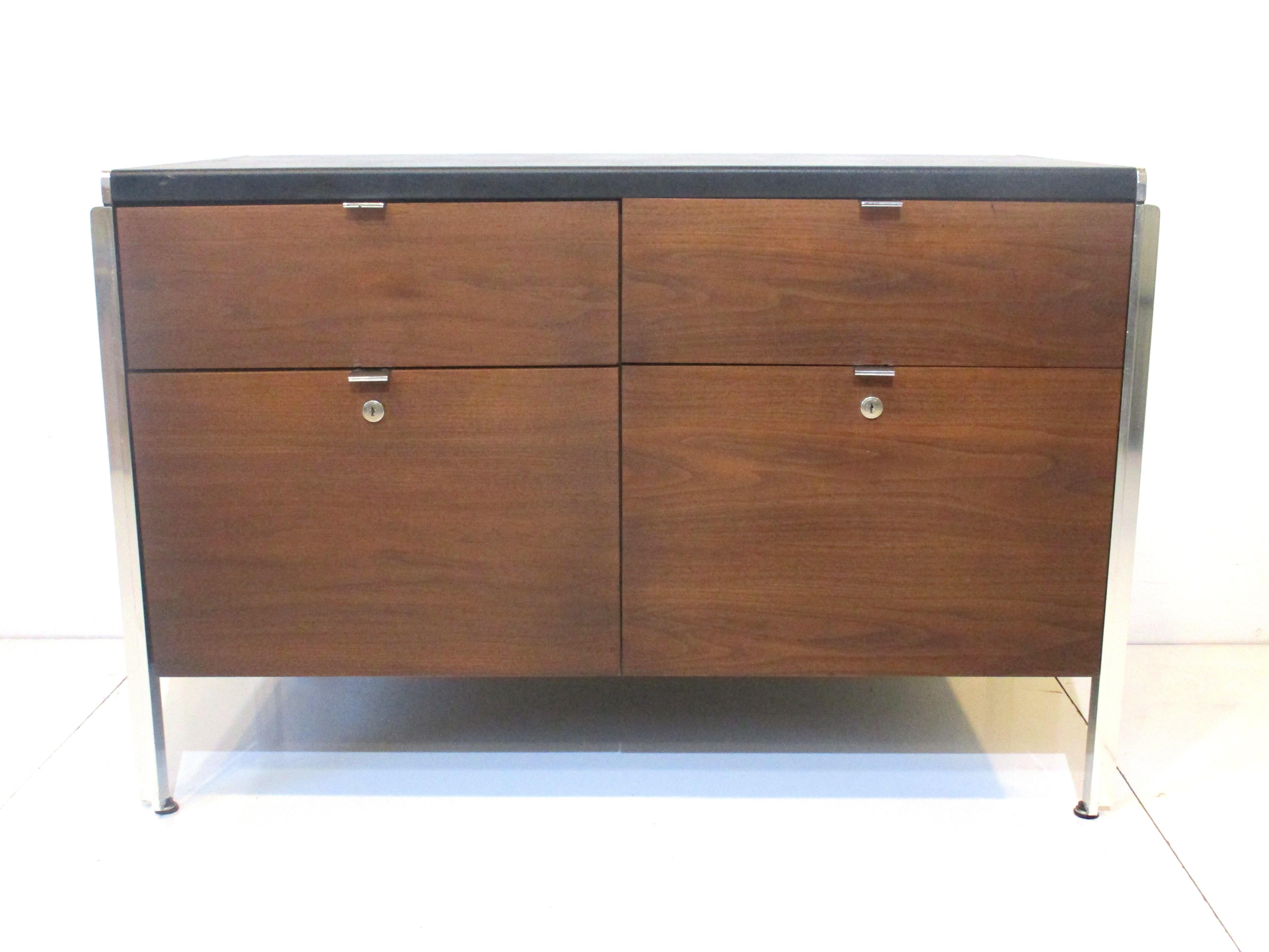 A very well crafted Mid Century small credenza in medium dark walnut with satin black leatherette top and great aluminum metal details to the legs and pulls . This  piece has two smaller upper drawers and two large file sized lower drawers and is