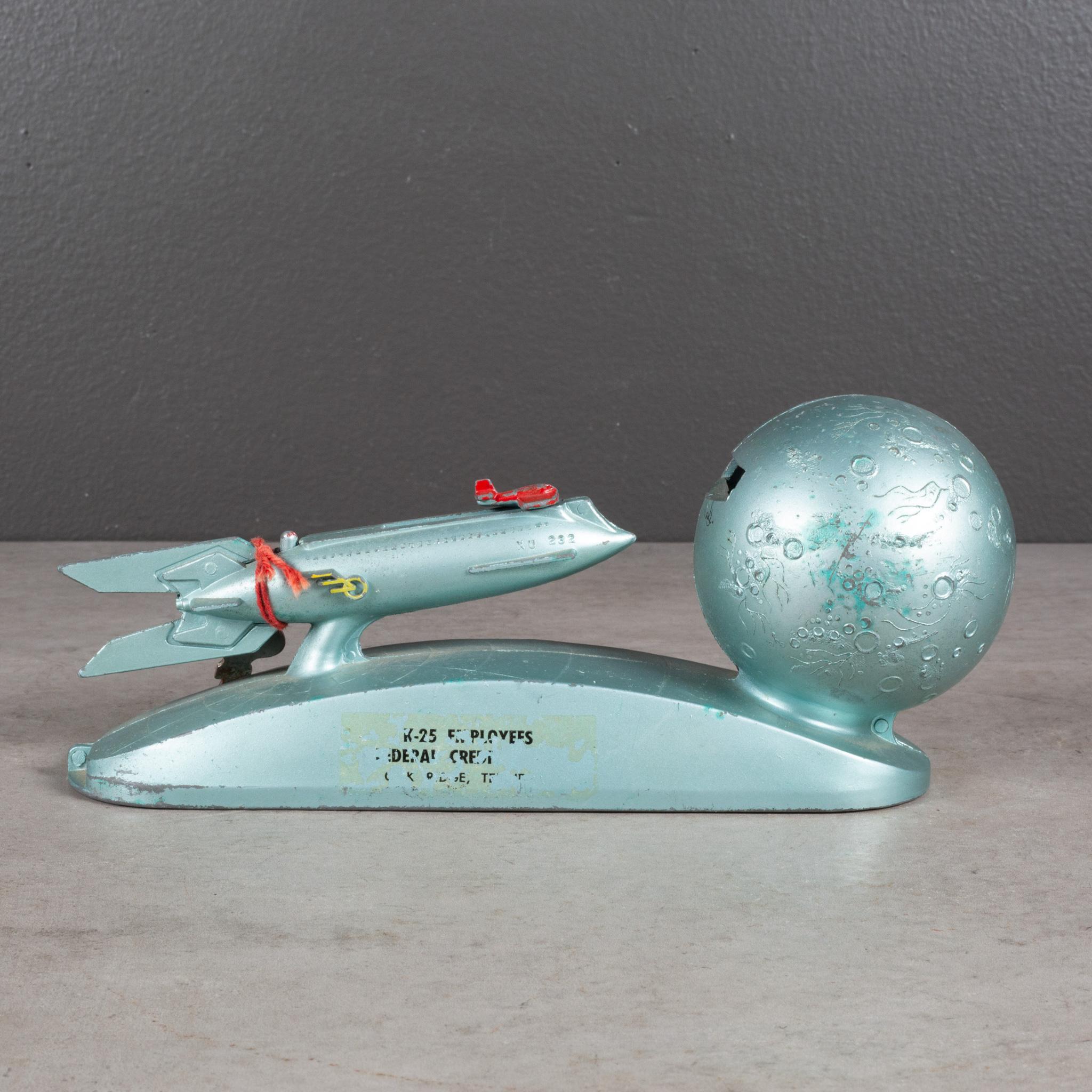 ABOUT
This metal, mechanical bank includes a red plane mechanism for launching coins from the rocket into the moon. Works properly. Includes key to unlock the bottom to retrieve the coins. 

    CREATOR Duro Mold and Mfg.
    DATE OF MANUFACTURE