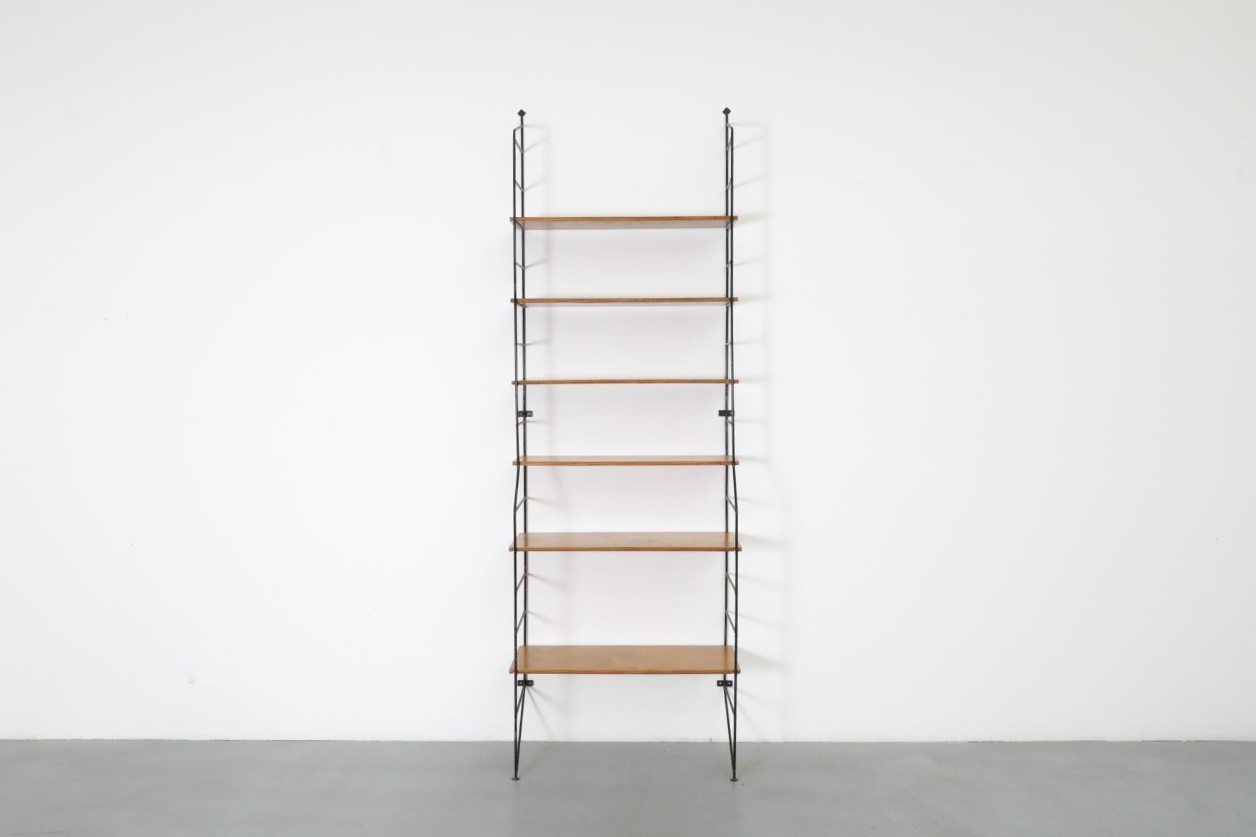 Mid-Century wall mounted bookshelf with black enameled wire frame and plywood shelves. The bottom two shelves are deeper than the top 4. In original condition with visible wear consistent with its age and use. Other similar bookshelves available,
