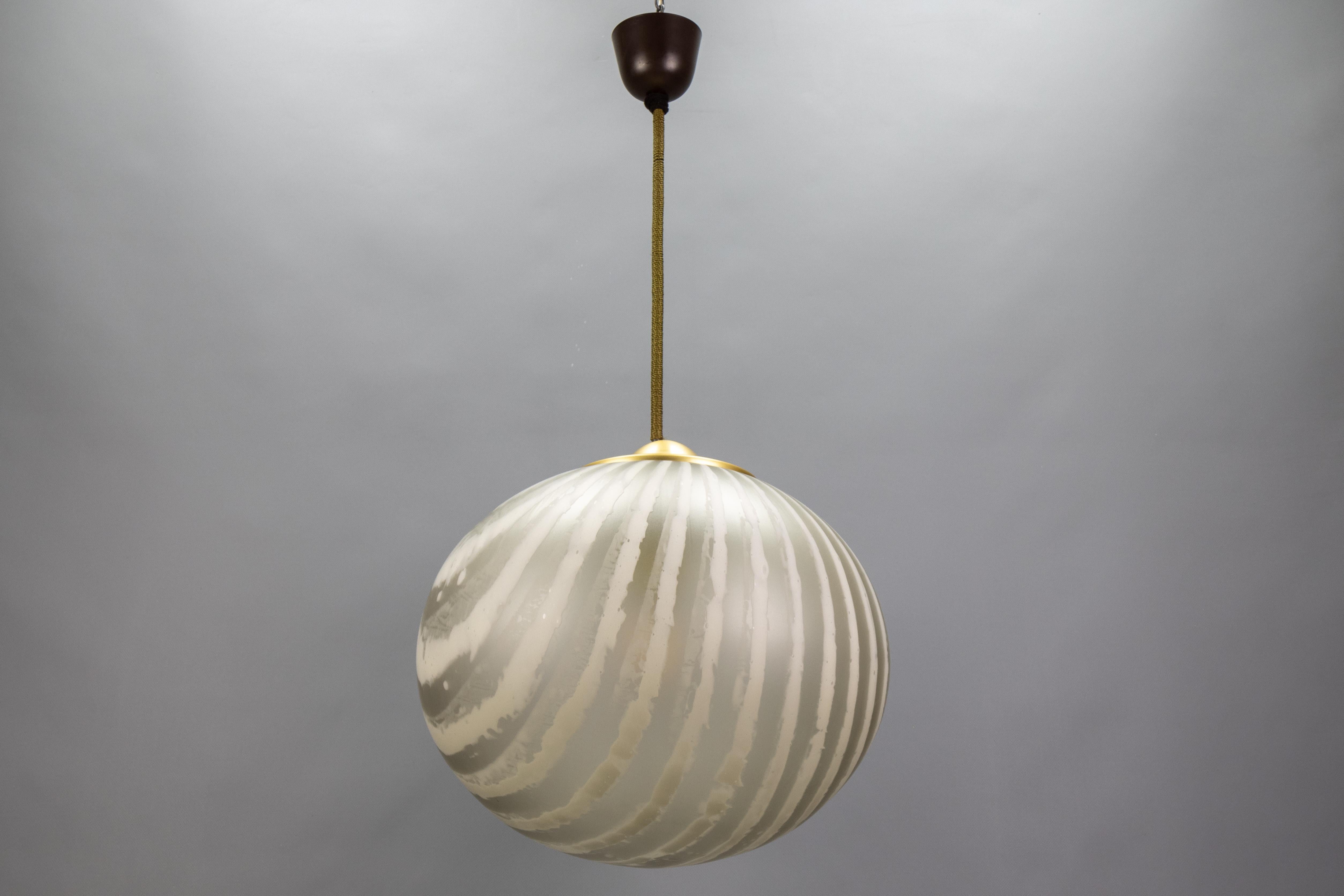 Suspension globe en verre rayé de Peill & Putzler, Allemagne, années 1970. Abat-jour soufflé à la main avec des bandes givrées et des bandes claires plus foncées qui créent des contrastes vibrants à la lumière. Raccord en laiton, couvercle en