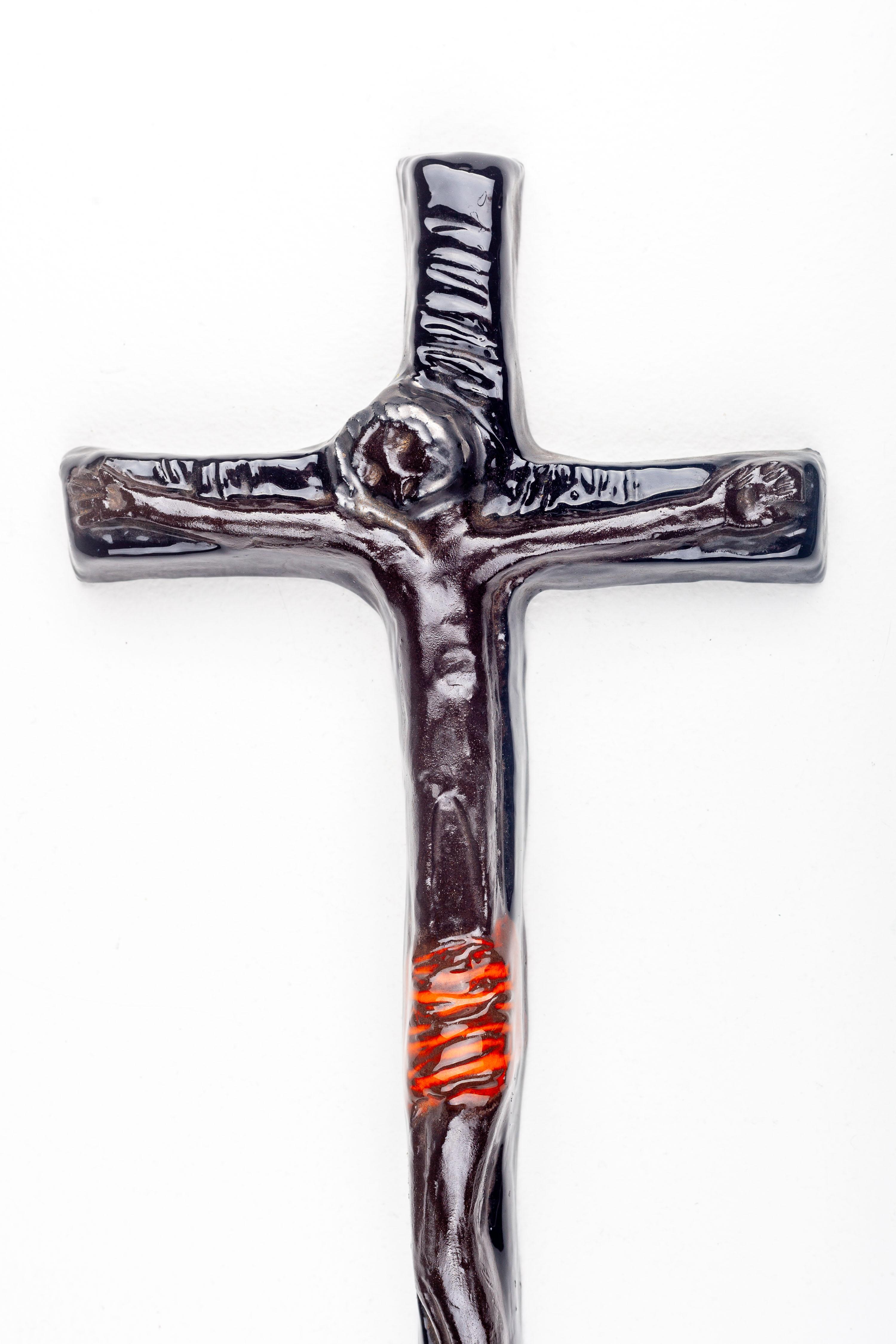 This mid-century modern wall crucifix exemplifies the innovative spirit of European studio art pottery from the 1950s to the 1970s. The piece is characterized by its organic, flowing lines and the contrast between the glossy, dark-toned glaze and