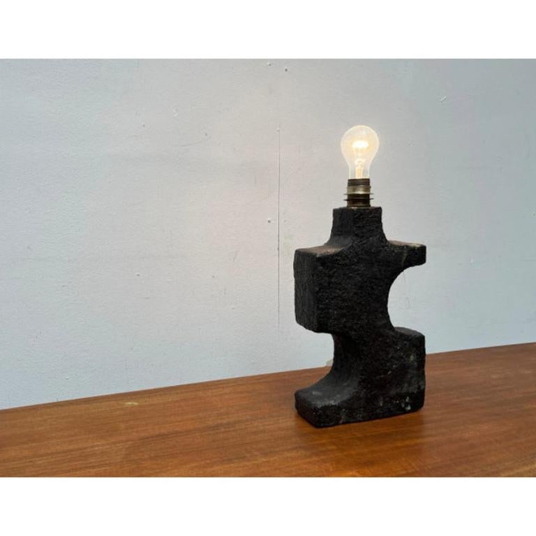 Mid Century Studio Pottery Table Lamp.

A brutalist design of imposing size. The lamp body is made of heavy ceramic and has a roughly structured surface. The shape is cut with wide curves on both sides. The frame has a simple holder for a standard