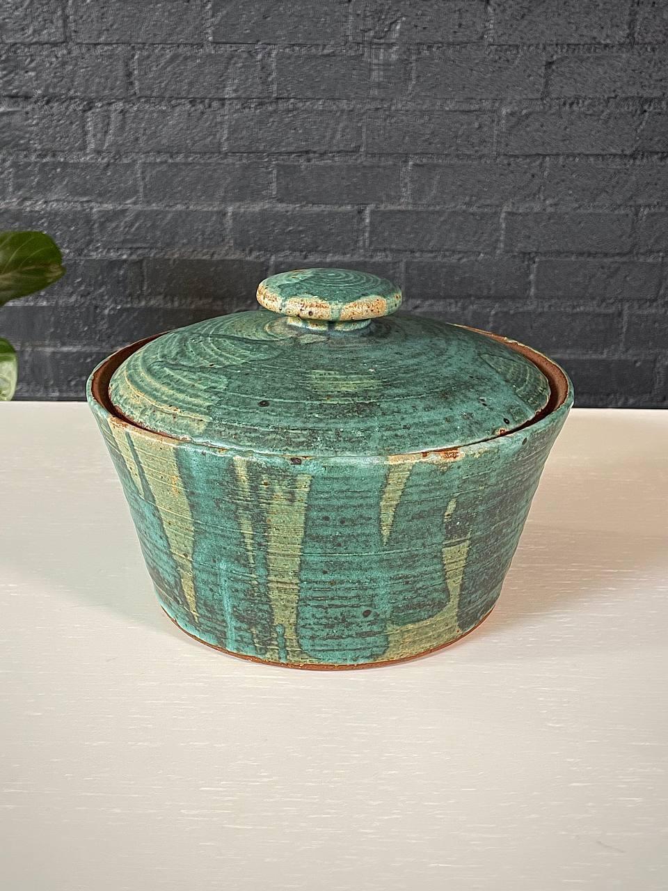 Ce vase à couvercle en poterie Studio du milieu du siècle, signé par l'artiste, présente une glaçure unique en son genre, avec des motifs verts dynamiques s'écoulant organiquement sur sa surface. La riche variation de tons et de textures reflète la