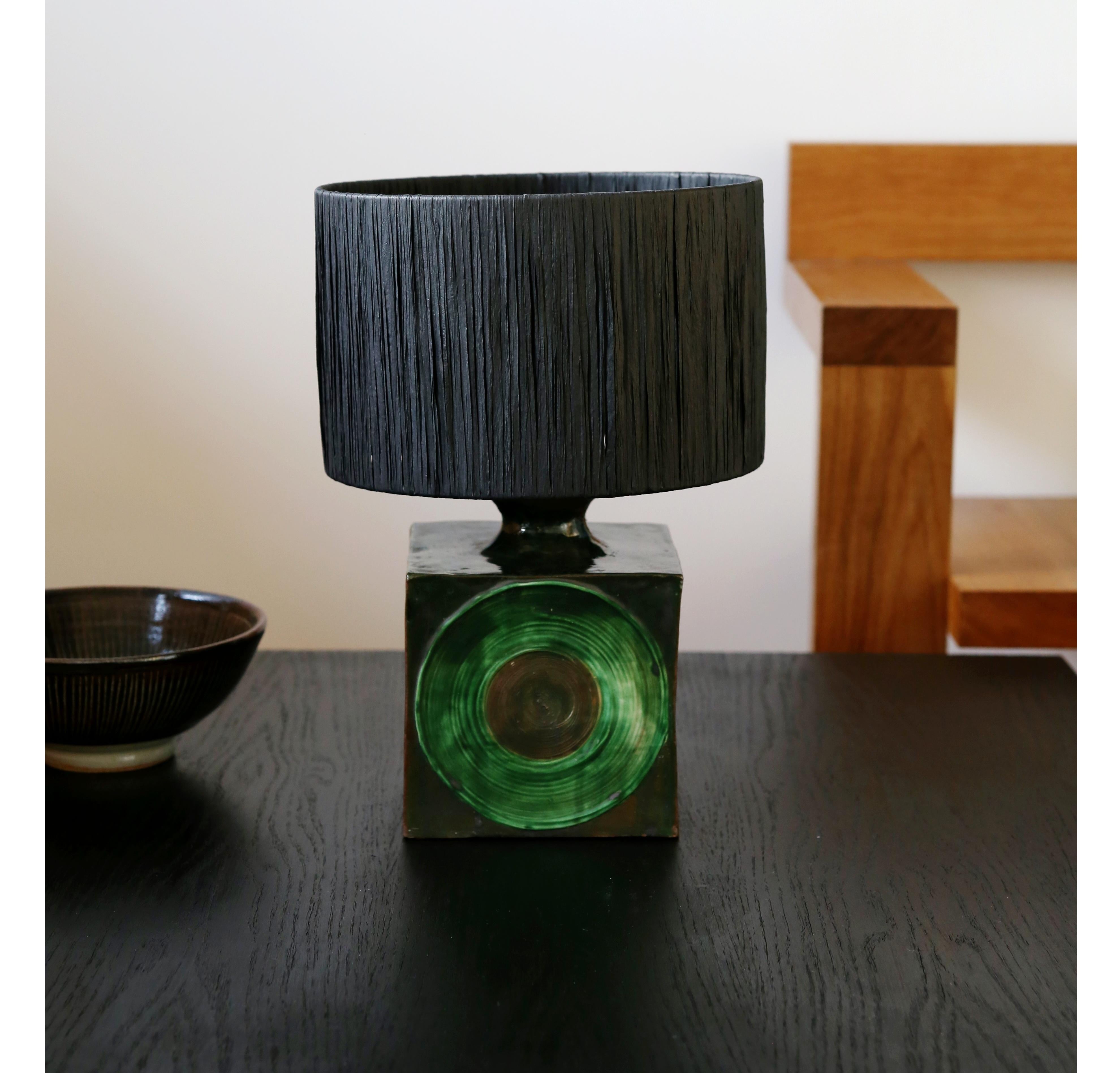 Fabulous 1970s statement studio pottery table lamp with a black raffia drum shade (the shade is new)

A heavy square lamp base with a brown and green over all mottled glaze and featuring a striking green lightly textured circle motif on the front of