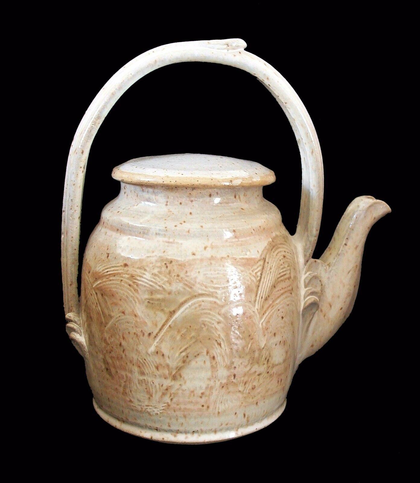 Midcentury stoneware studio pottery teapot - hand carved/scraped decoration to the exterior - gloss cream glaze - dramatic integrated handle - separate lid - indistinctly signed on the base - Canada - circa 1970s.

Excellent vintage condition - no