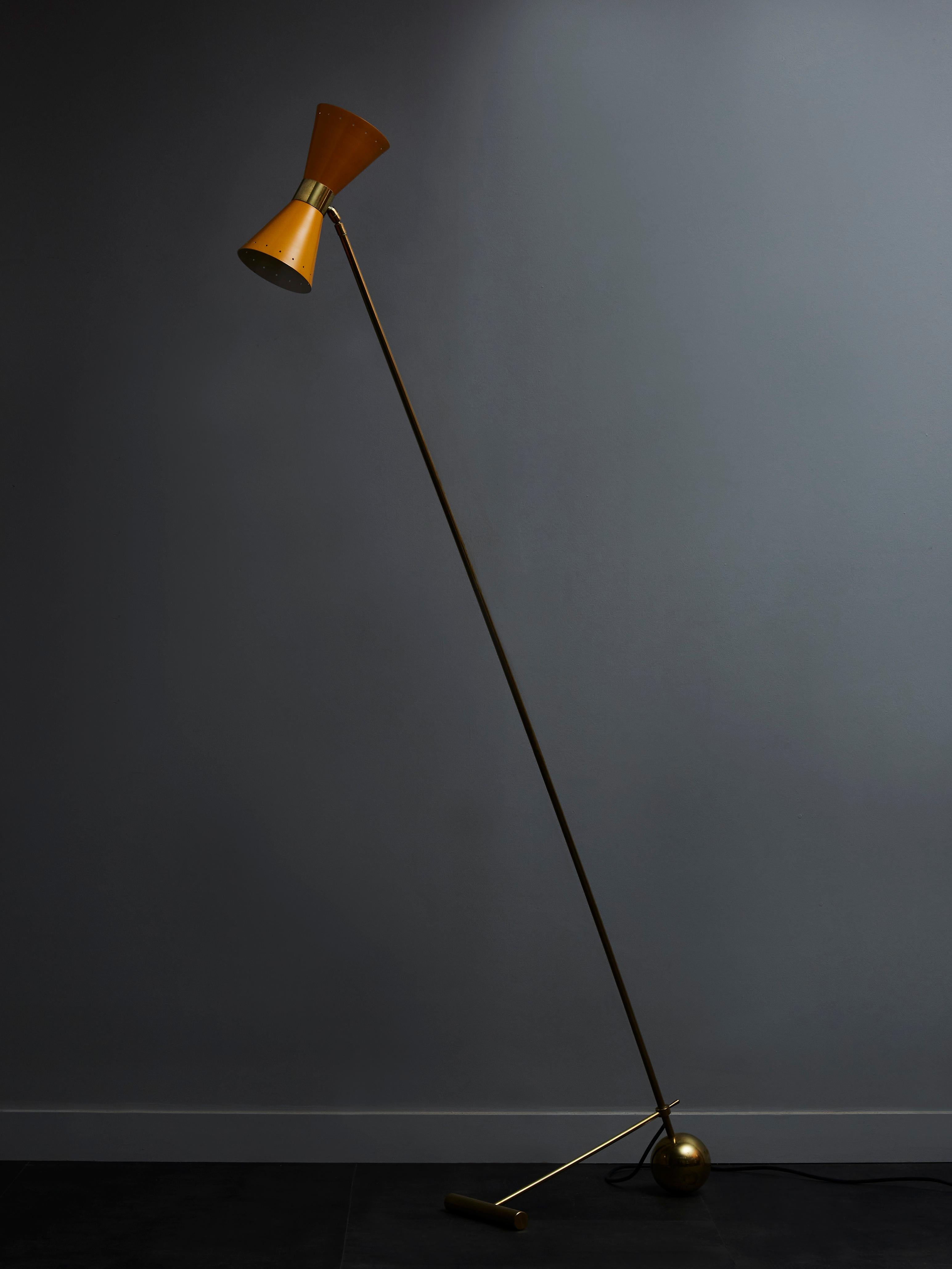 Midcentury style floor lamp made of a long brass arm hold in place by a geometrical foot and holding two yellow cones each hosting a single light.