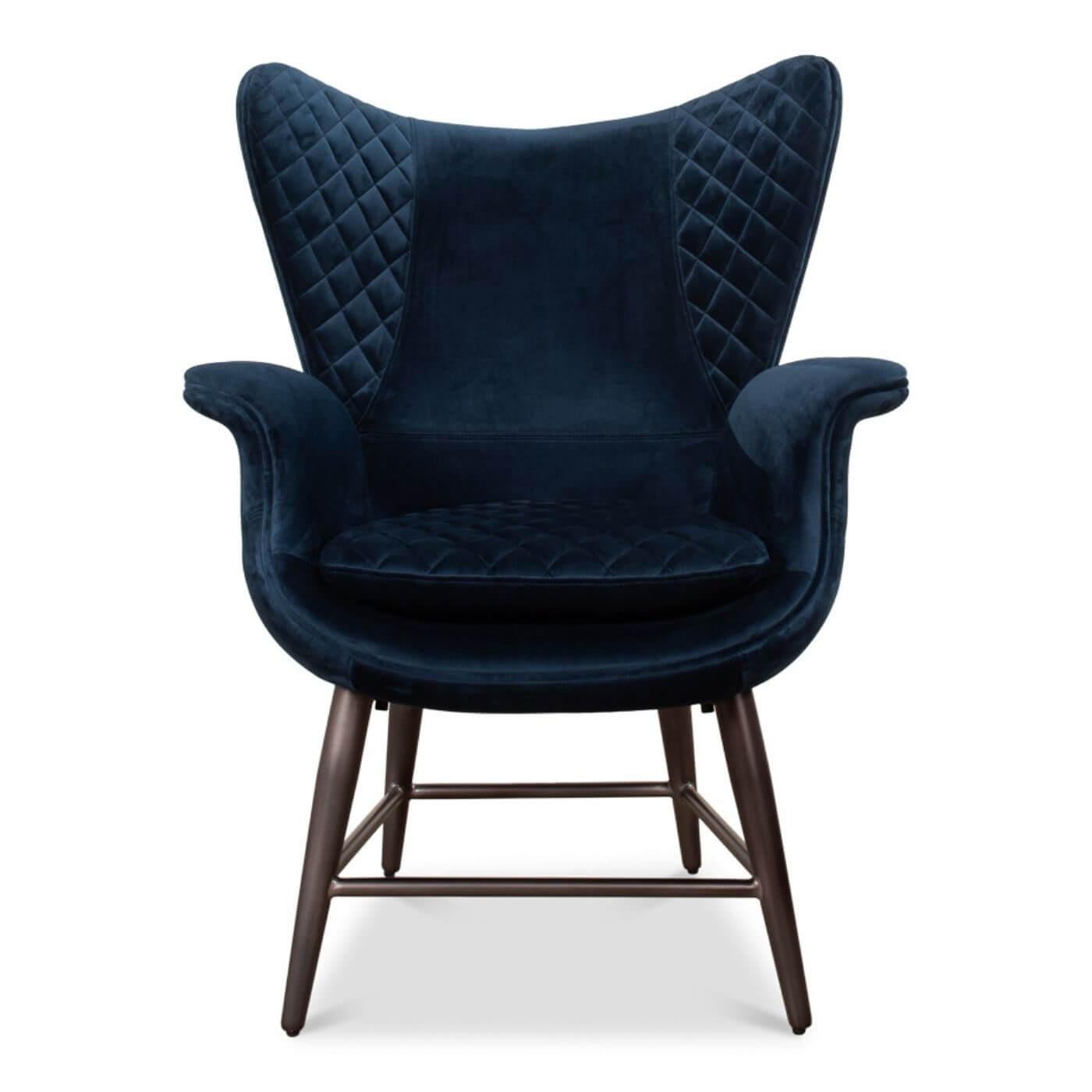 A mid-century style velvet armchair with navy blue velvet upholstery, with a diamond-quilted interior and topstitched seams. It features a curve-around design and rests on rich brown finished splayed legs. 

Dimensions: 32