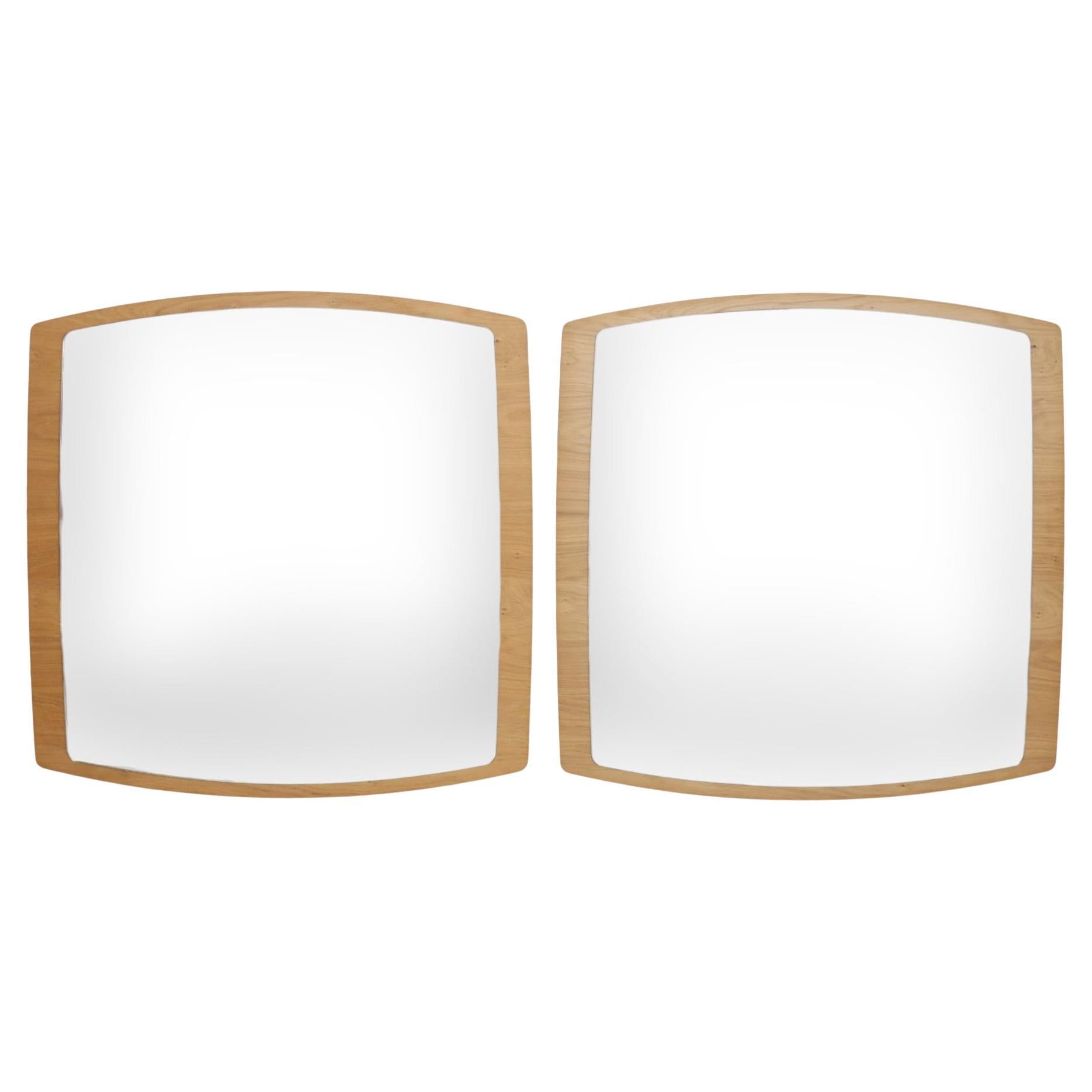 A pair of mid-century style wall mirrors. Rectangular mirrors with gently bowed edges are mounted on maple frames with a natural finish. Frames are beveled in angular forms away from the wall. Mounts in the back allow the mirrors to be hung