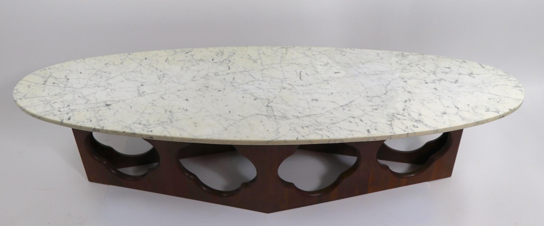 Very chic midcentury surfboard top coffee, cocktail table have a thick (7/8 inch ) Italian marble top, which rests on a six sides wood base with pierced quatrefoil openings. Base reads as a diamond form, however actually has six sides, four long