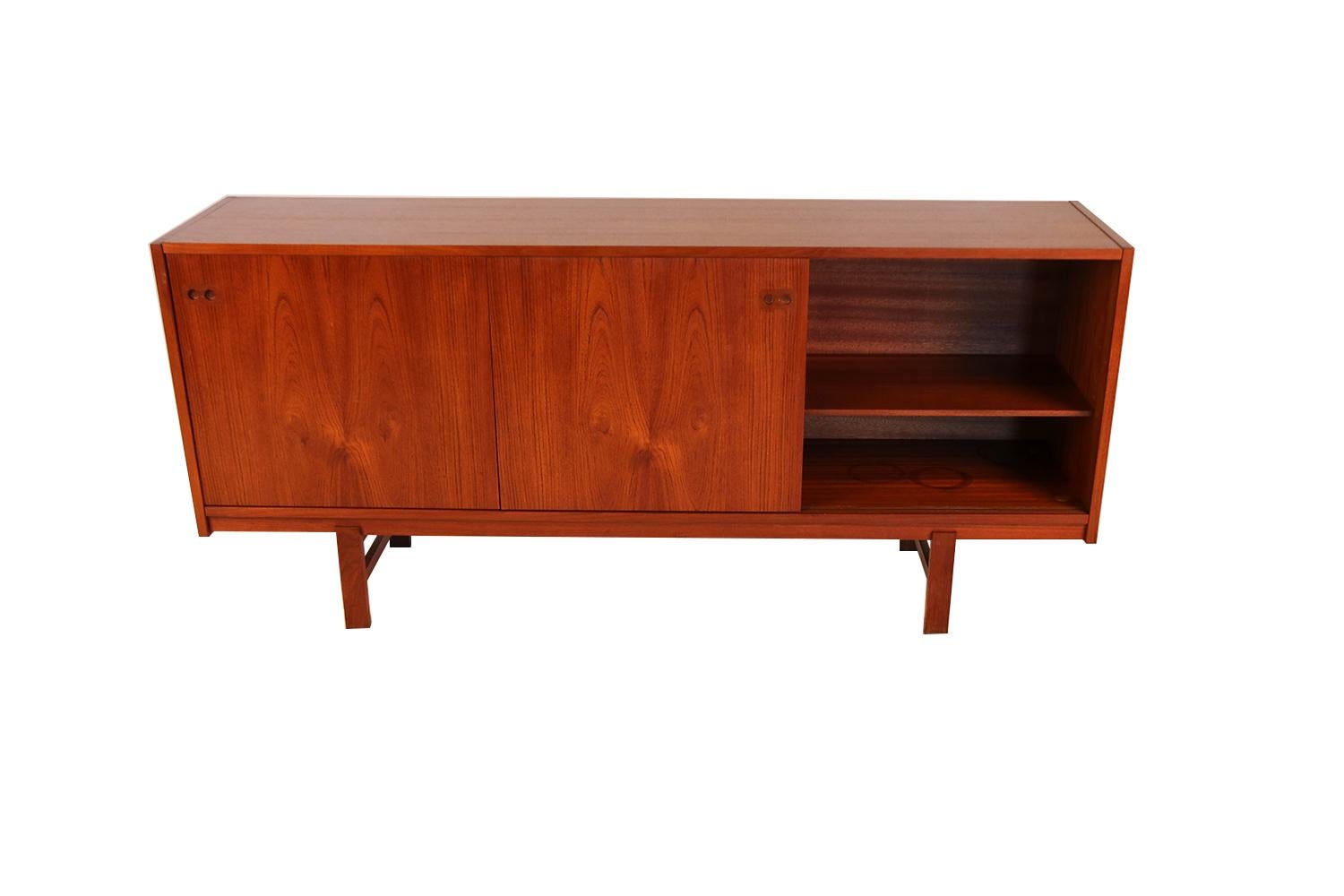 Gorgeous midcentury Danish, beautifully grained, teak, sliding door credenza/sideboard made in Denmark. Each cabinet features a sliding door with inset sculpted circular pulls, opening to reveal a central cabinet with three felt lined, dovetailed
