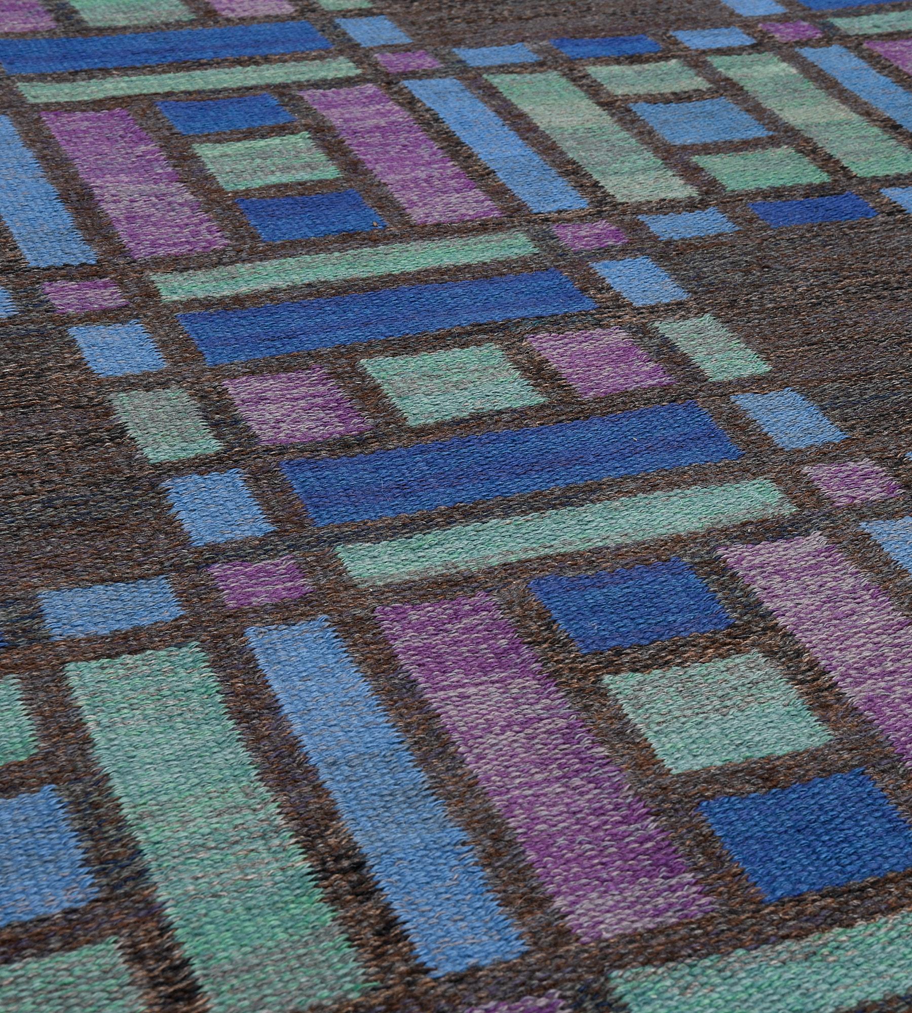 This mid-century Swedish flatweave rug has a charcoal-brown field with two vertical columns and three horizontal rows of pistachio-green, sky-blue, light blue and purple small spaced square and rectangular colors, which together create a