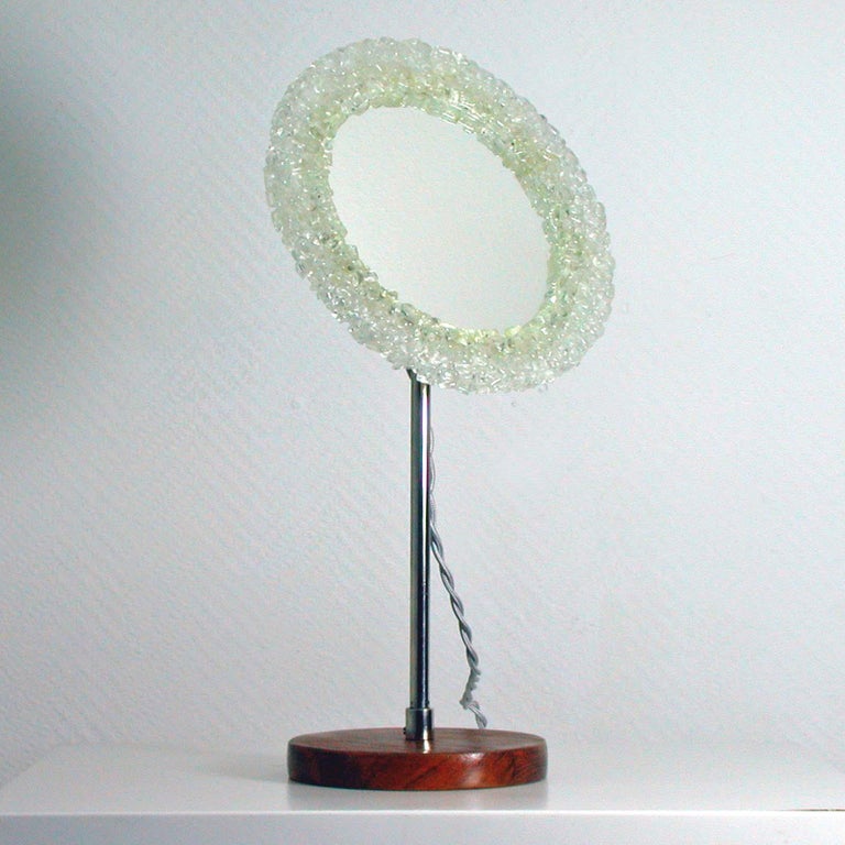 This round vanity mirror was made in Sweden in the 1960s-1970s. It has got a teak base, a chrome mirror rod and a backlit acrylic frame. The frame is adjustable.

The mirror requires a small E14 screw on bulb. It has been rewired with silk silver
