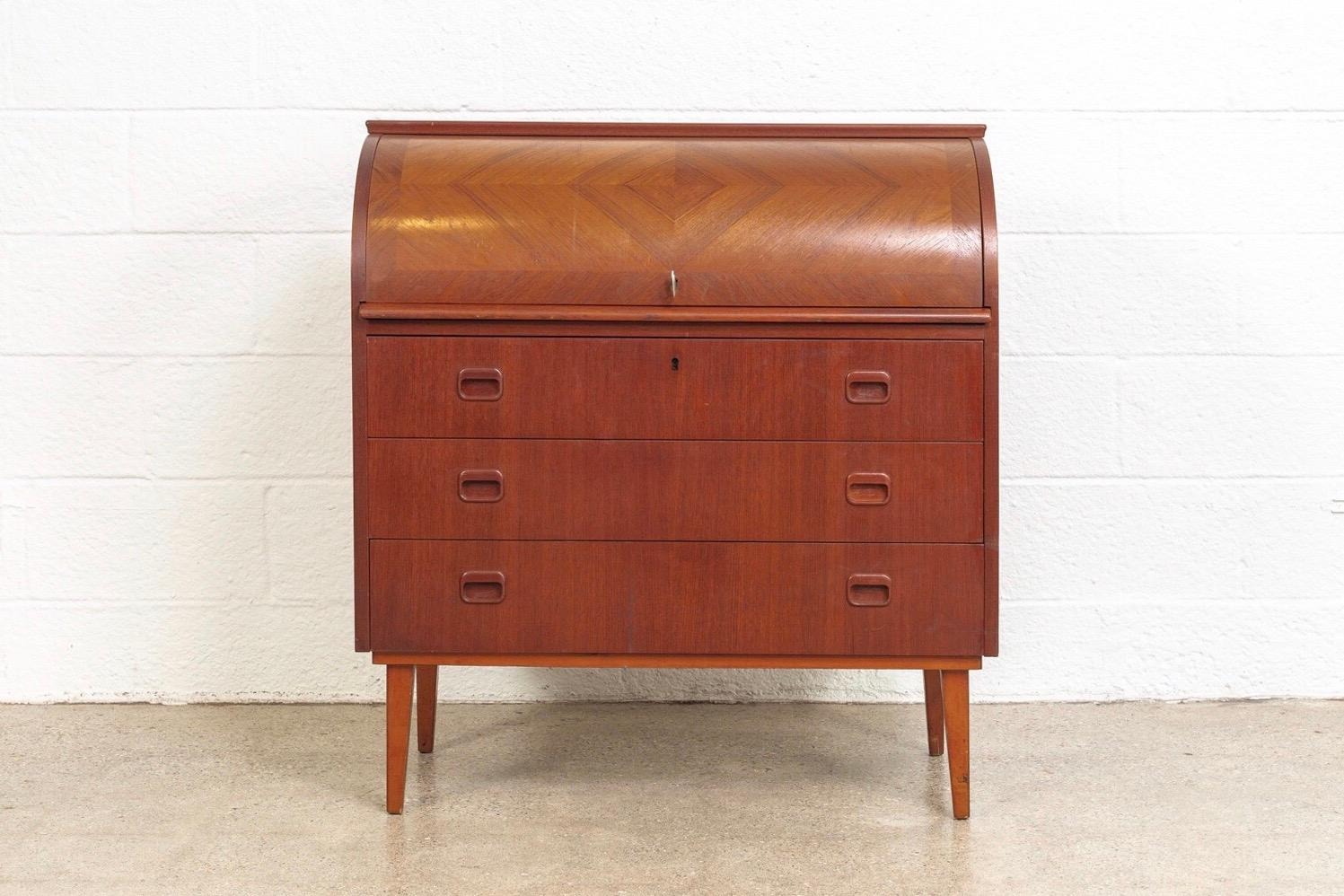 This iconic midcentury Swedish modern Egon Ostergaard teak cylinder rolltop secretary desk cabinet is circa 1970. The Classic Scandinavian Modern design has clean Minimalist lines and features a beautiful inlaid diamond-patterned rolltop surface.
