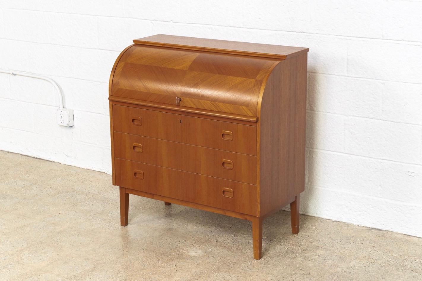 This iconic midcentury Swedish modern Egon Ostergaard teak cylinder rolltop secretary desk cabinet is circa 1970. The Classic Scandinavian modern design has clean Minimalist lines and features a beautiful inlaid opposing-grain pattern rolltop