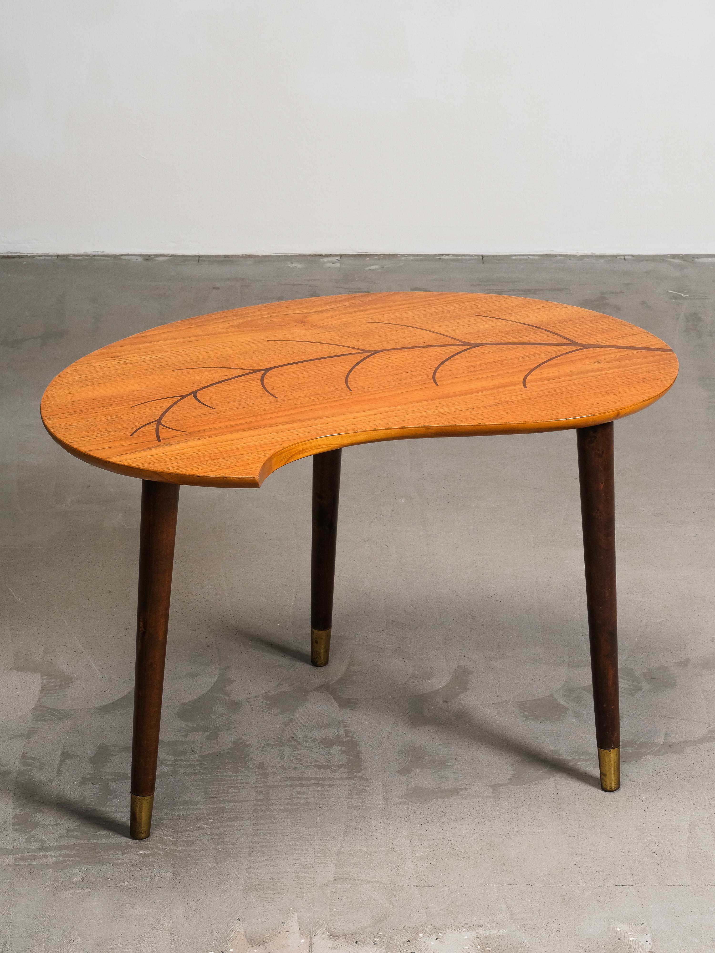 A Swedish mid-century coffee table with a leaf-shaped teak top, decorated with an intarsia inlay in the form of a branch and leaves. The organic kidney-shaped form reflects the playful experimentation of 1950’s design, where natural motifs were