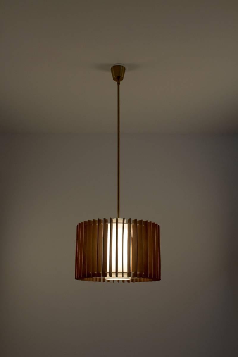 Rare pendant in brass, glass, wood and plastic by Hans-Agne Jakobsson.
This pendant features one light source surrounded by a shade in opaline glass. The top and bottom plates of the lamp are made of acrylic, and are held together by pieces of