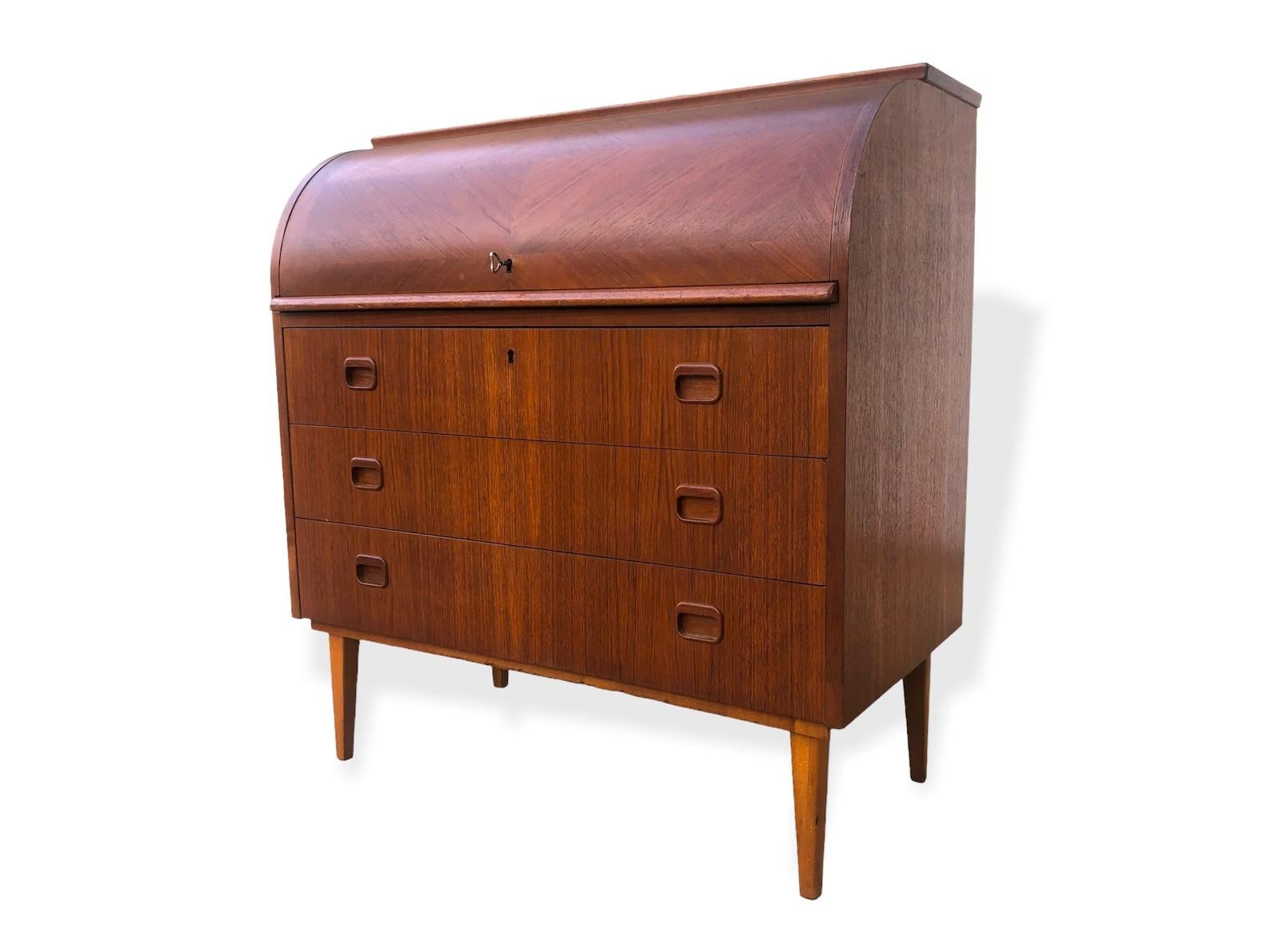 This iconic midcentury Swedish modern Egon Ostergaard teak cylinder rolltop secretary desk cabinet is circa 1960. The Classic Scandinavian Modern design has clean, Minimalist lines and gentle curves. Wood tone is deep and rich with beautiful natural