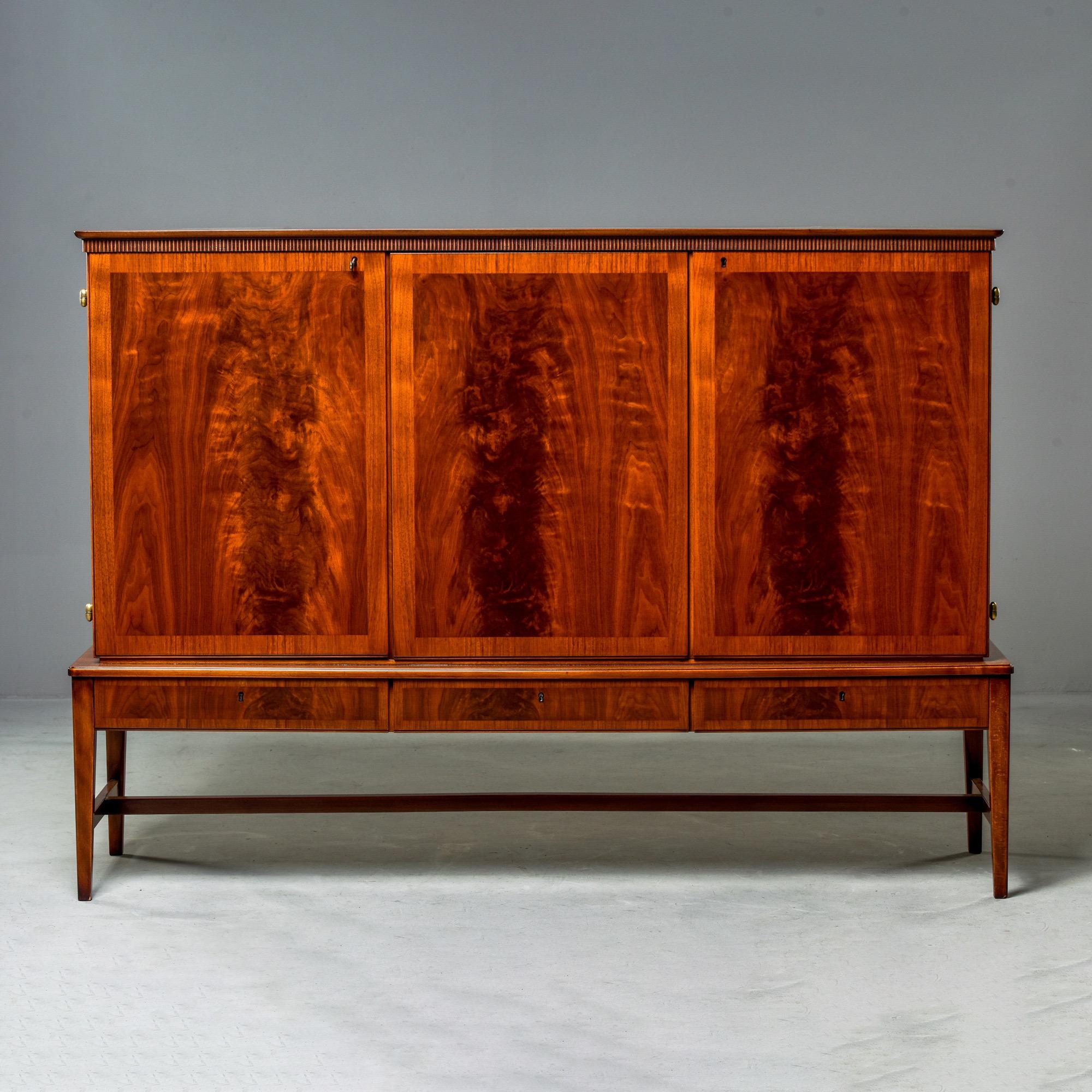 Swedish tall walnut credenza, cabinet-on-stand or buffet, circa 1960s. Top has two locking hinged doors with figured walnut panels and decorative cross-banded edges. Inside is large compartment with two adjustable shelves. The small compartment