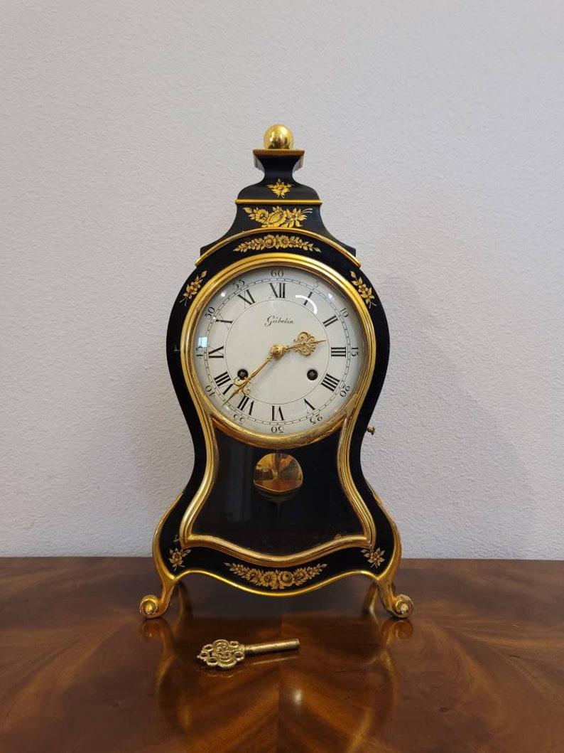 From the House of Gübelin, an elegant mid-20th century Swiss mantel clock. Reminiscent of lavish French Louis XV taste, the vintage clock features a violin shaped parcel gilt wooden case, surmounted by round finial, fitted with dome glazed dial