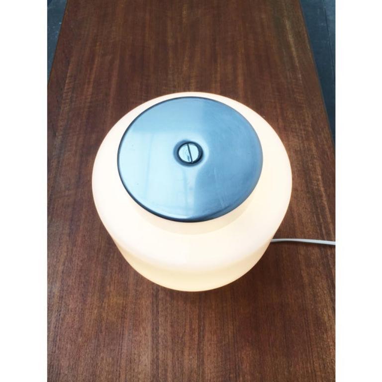 Table lamp from the Swiss manufacturer Temde.

A minimalist design. The lamp shows a simple cylindrical shape. The aluminum cylinder is pierced in the upper third by a diffuser of opal glass. A striking detail is formed by the large slotted screw on