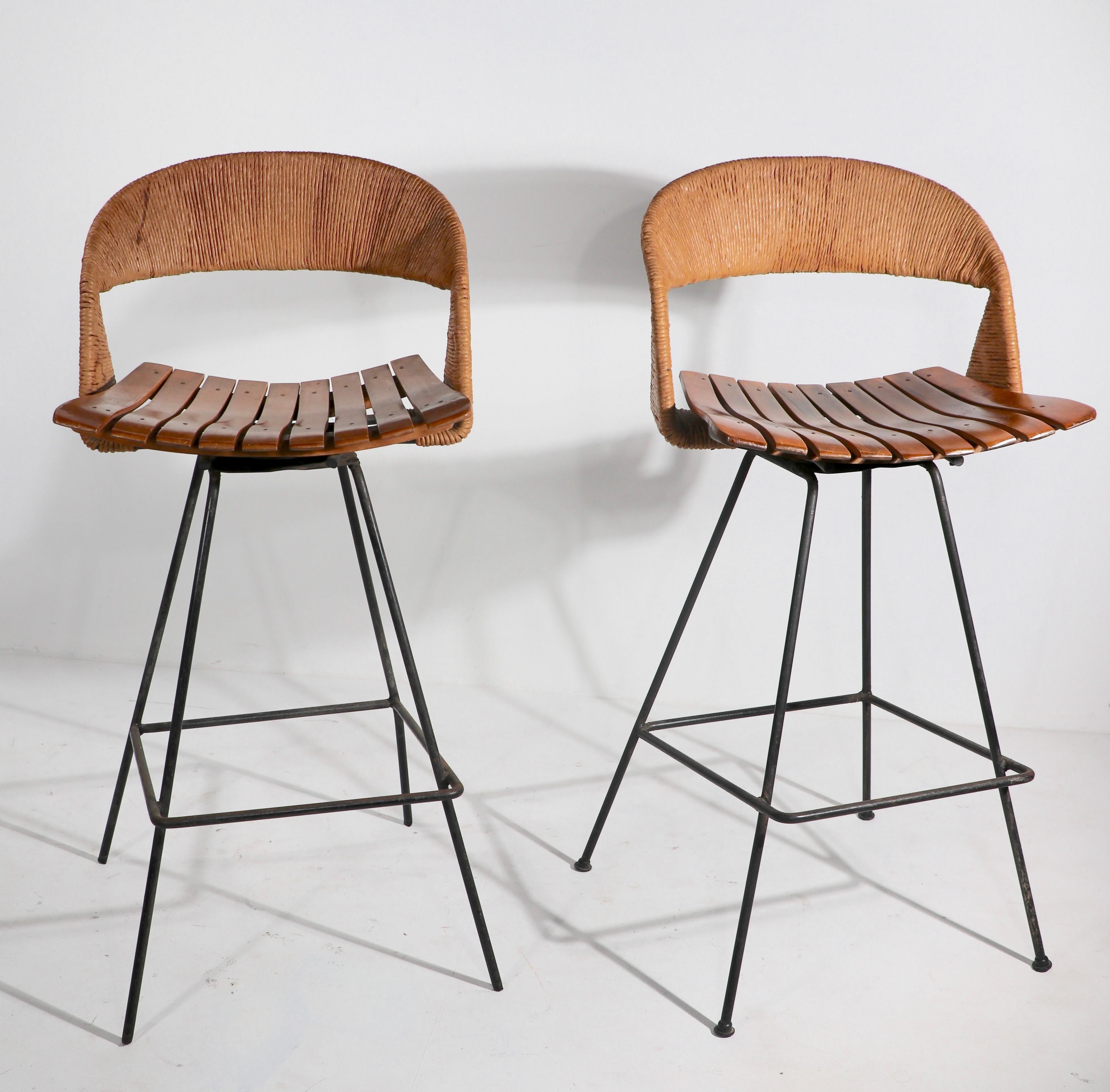 Rare swivel bar stool by Arthur Umanof for Raymor, in good original condition. The stool features a cord wrapped backrest, wood slat seat, and wrought iron base. The stool has some imperfections as follows> One back leg is slightly bent, the plastic