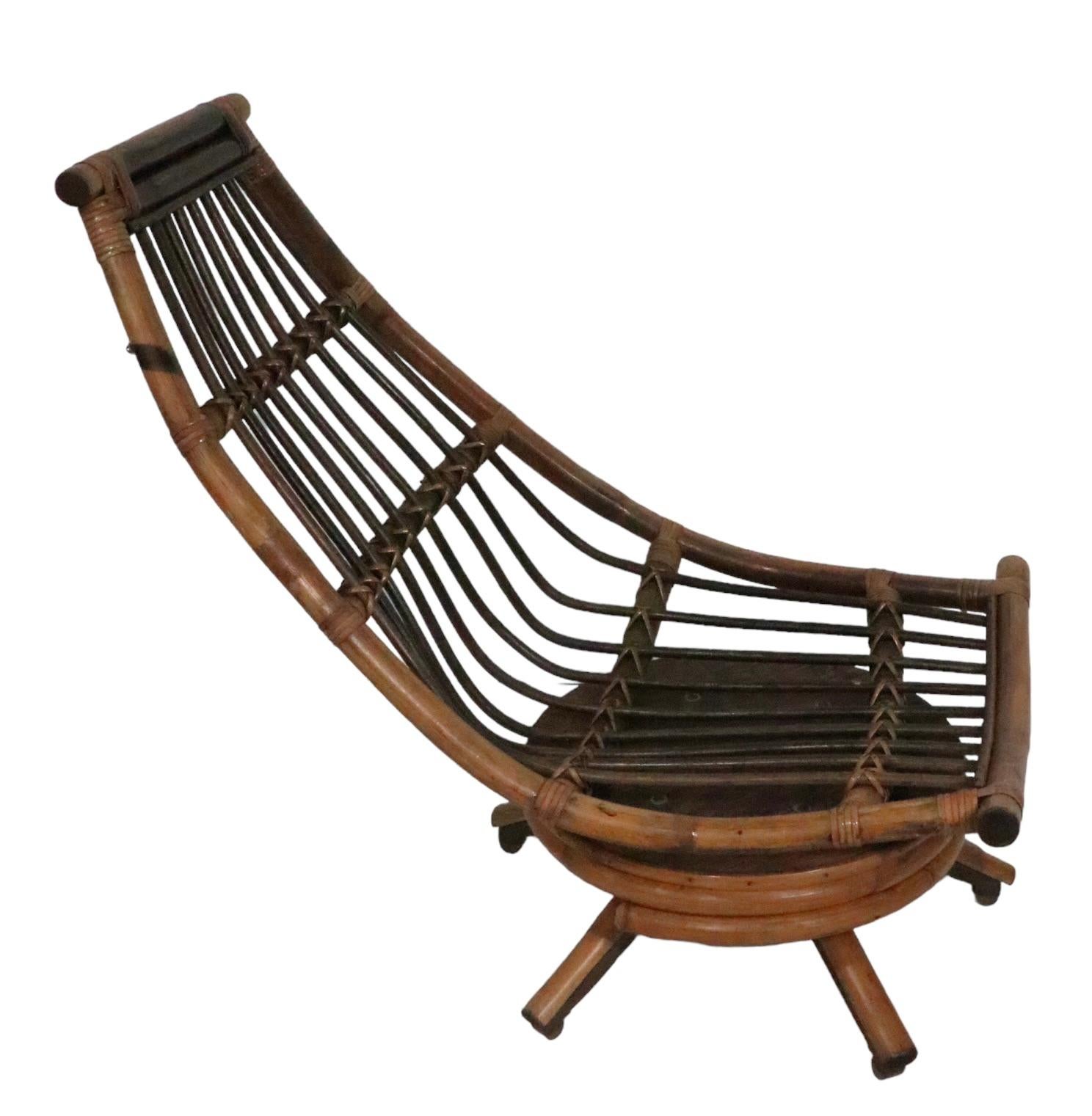 Chic midcentury bamboo platform lounge chair, having a banana shaped seat, which swivels and tilts on the circular plinth base. The chair includes a black vinyl seat pad, pad is usable as is, but shows significant wear, please see images. 
Unusual