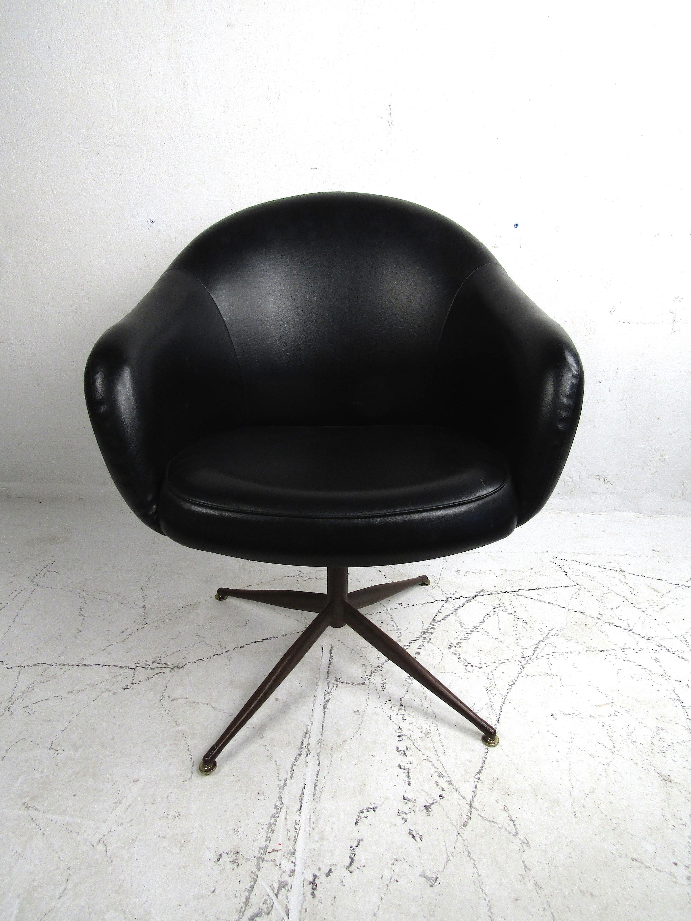 Stylish midcentury swiveling club chair manufactured by the Baumritter corporation in the 1960s. This chair is covered in a vintage black faux-leather upholstery and is attached to a swiveling base. Interestingly, the metal base has etchings to give