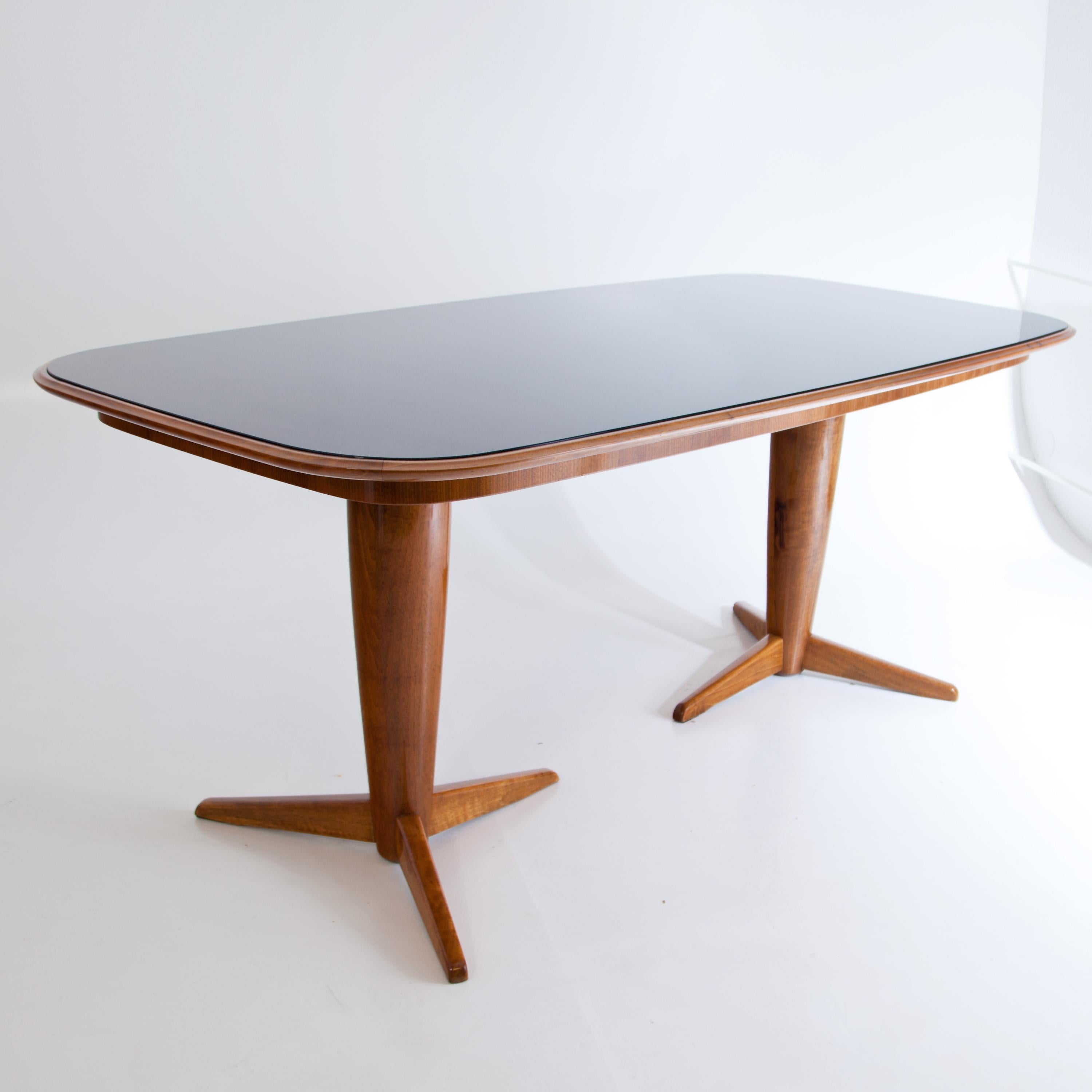 Midcentury table with rectangular table top with rounded corners. The table stands on two legs with three feet each. The table top is colored in black and covered with a glass top.