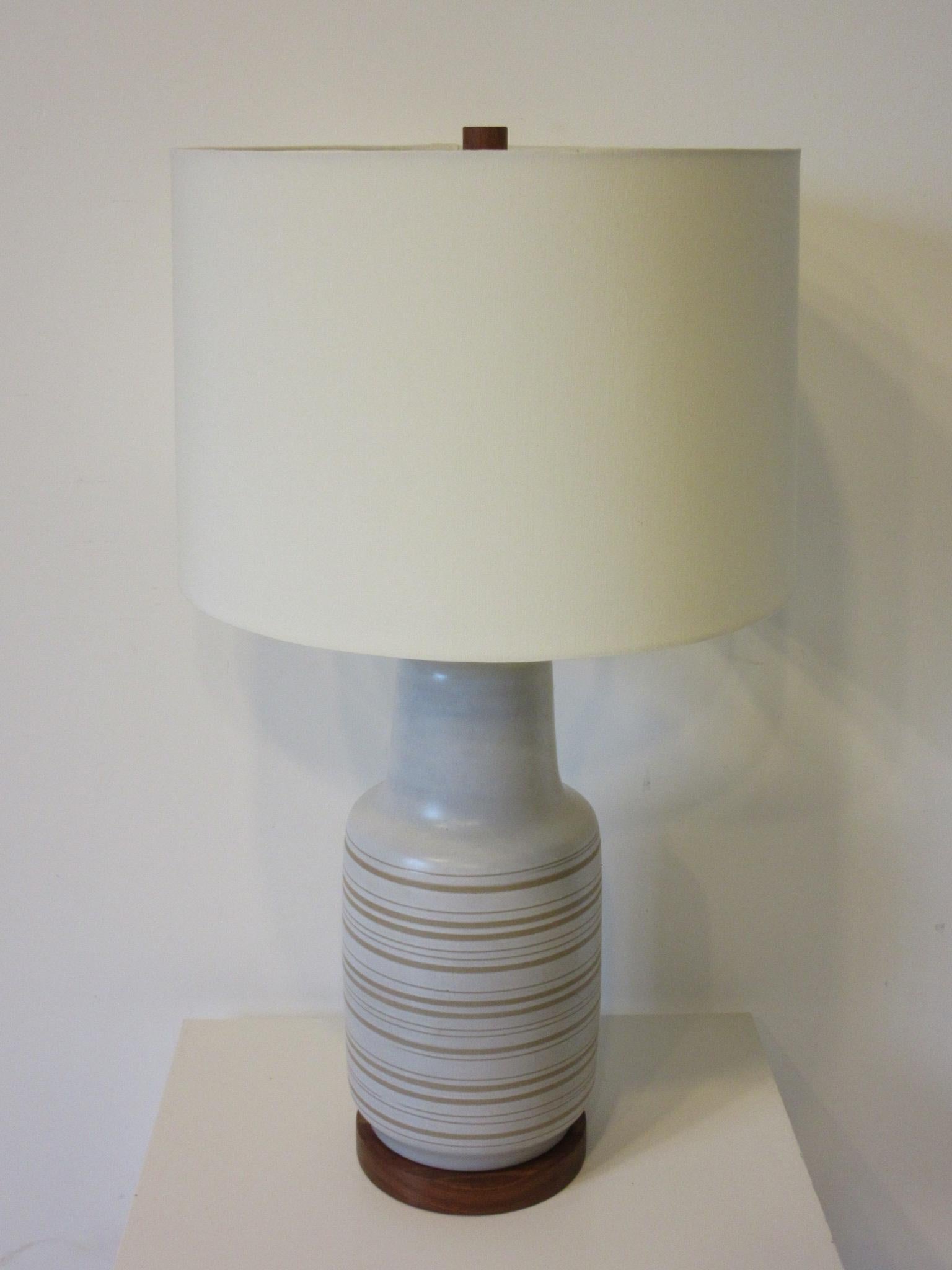 A midcentury pottery table lamp in cream having incised sand tone color stripes with original teak wood base and matching finial. The original shade has been replaced with a high end up to date light cream colored linen shade, the lamp retains the