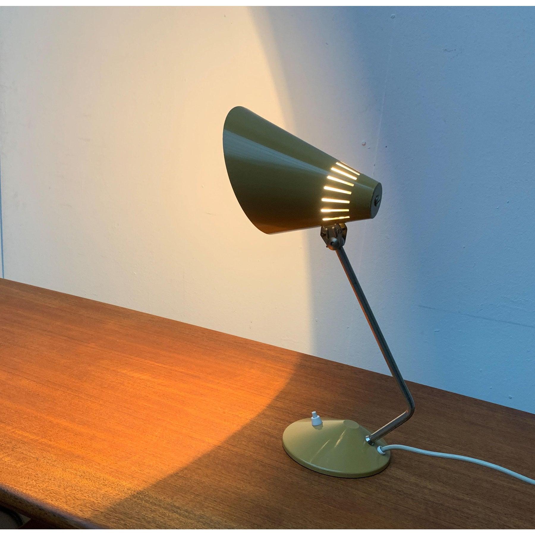 Lampe de table Mid Century.

L'abat-jour de la lampe est conçu en forme de cône. Il peut être aligné par l'intermédiaire d'une articulation. La tige angulaire de la lampe, qui relie la base et l'abat-jour, est frappante. L'abat-jour et la base sont