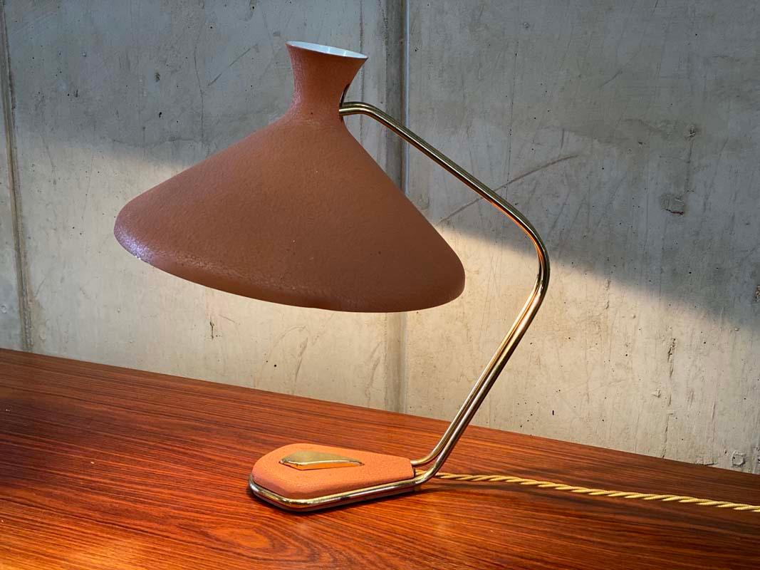 An elegantly curved table lamp in the style of Louis C. Kalff. 
It captivates with the extravagant design language of the 1950s.
The crackled lacquer finish in a beautiful salmon tone and the brass lamp base make the lamp look feminine and fresh.